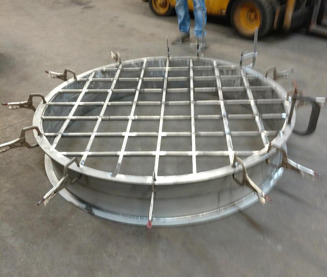 Large circular metal frame with grid pattern, secured by clamps, on a workshop floor.