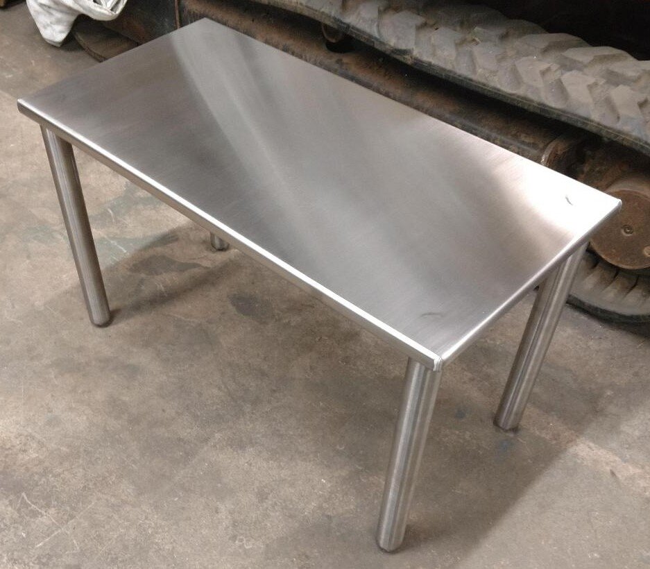 Stainless steel work table with four legs on a concrete floor.
