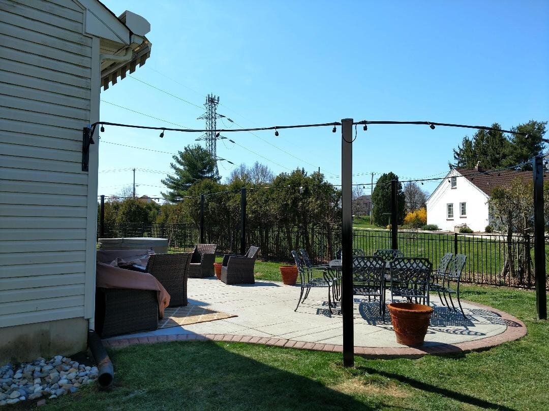 Outdoor patio with chairs, table, planters, and string lights in a backyard setting.