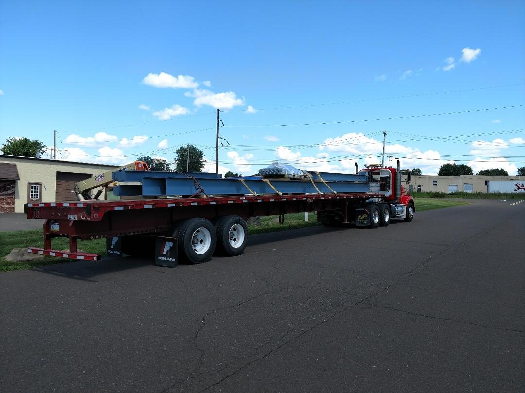 Flatbed truck carrying steel beams parked on a road under a blue sky.