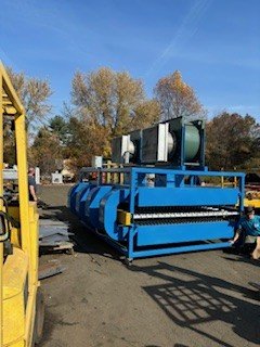 Large industrial machinery outdoors with blue housing and mechanical components, situated on an industrial site with trees in the background.