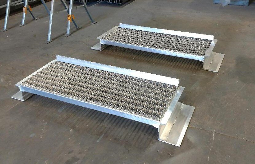 Two metal stair treads on a workshop floor, featuring diamond-patterned grating.