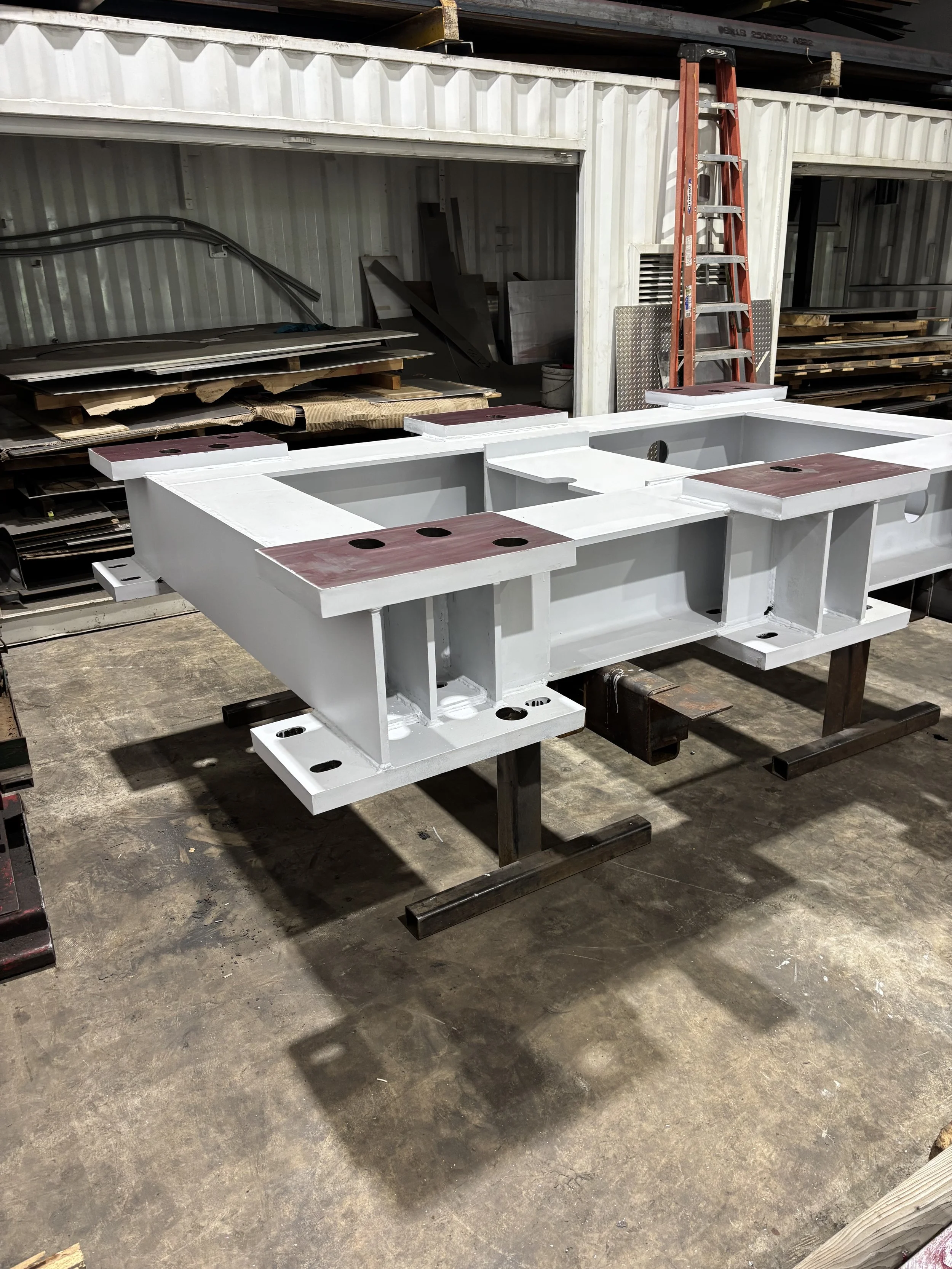 A white metal structure with wooden and metal components, supported by industrial stands, in a workshop or industrial setting.