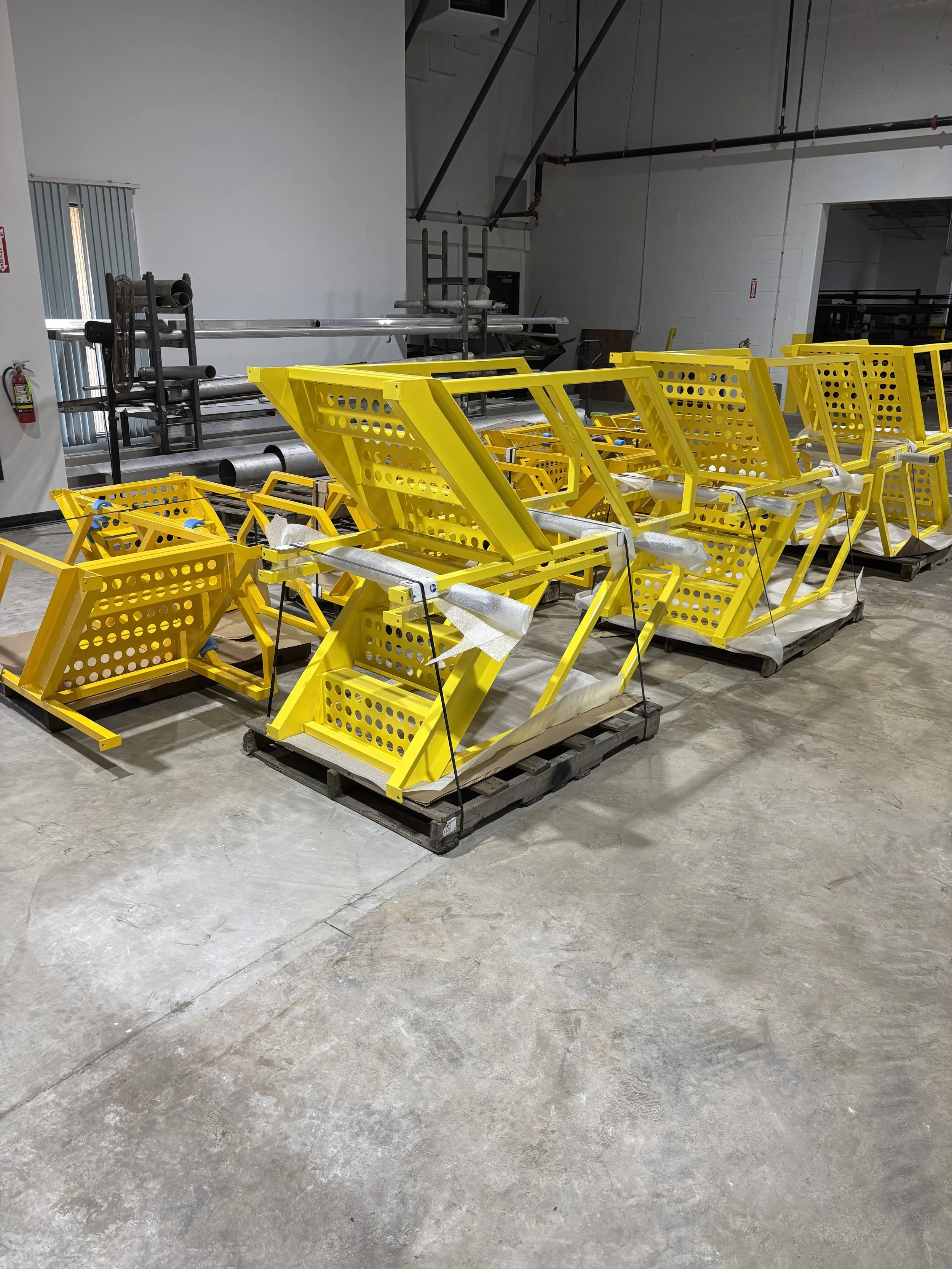 Stacked yellow metal safety barriers with holes, organized on pallets inside a warehouse.