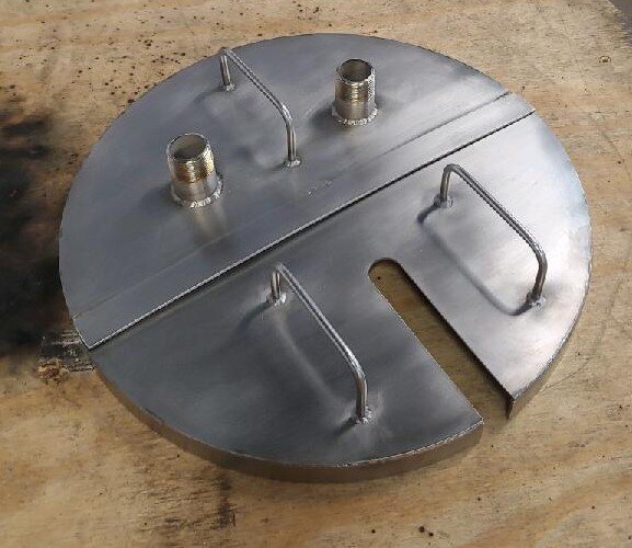 Metal circular plate with handles and threaded connectors used for industrial applications, placed on a wooden surface.
