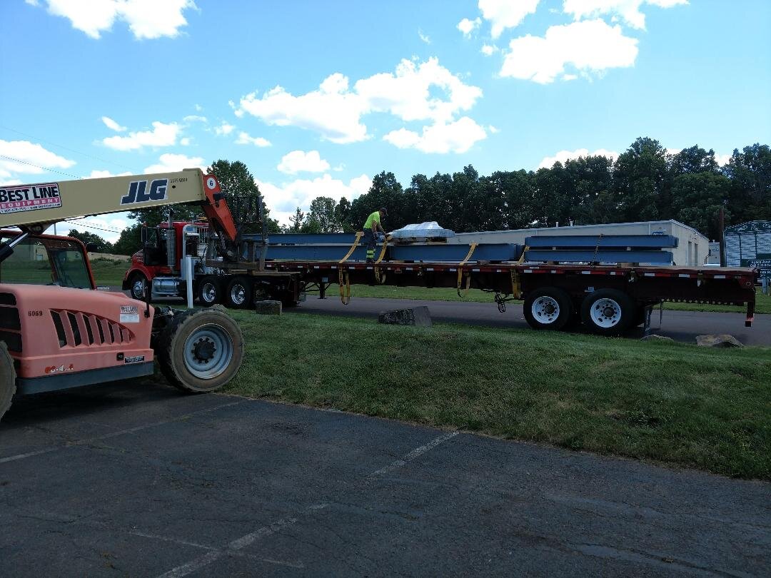 Forklift and truck with flatbed trailer carrying steel beams in a yard