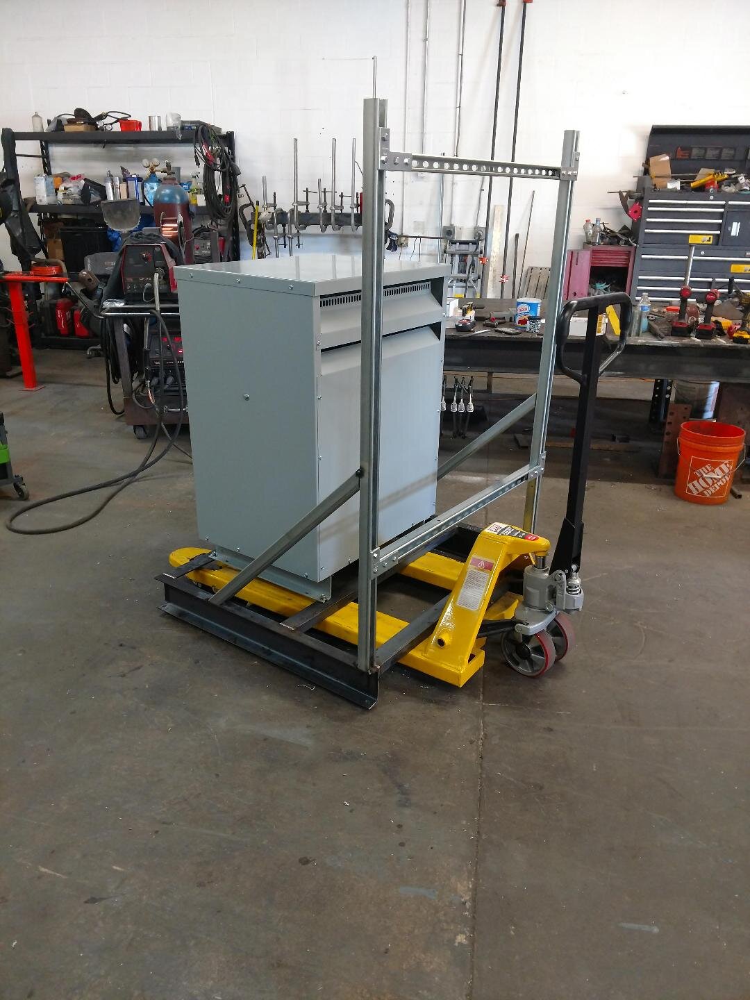 A workshop with a metal cabinet on a yellow pallet jack, surrounded by various tools and equipment.