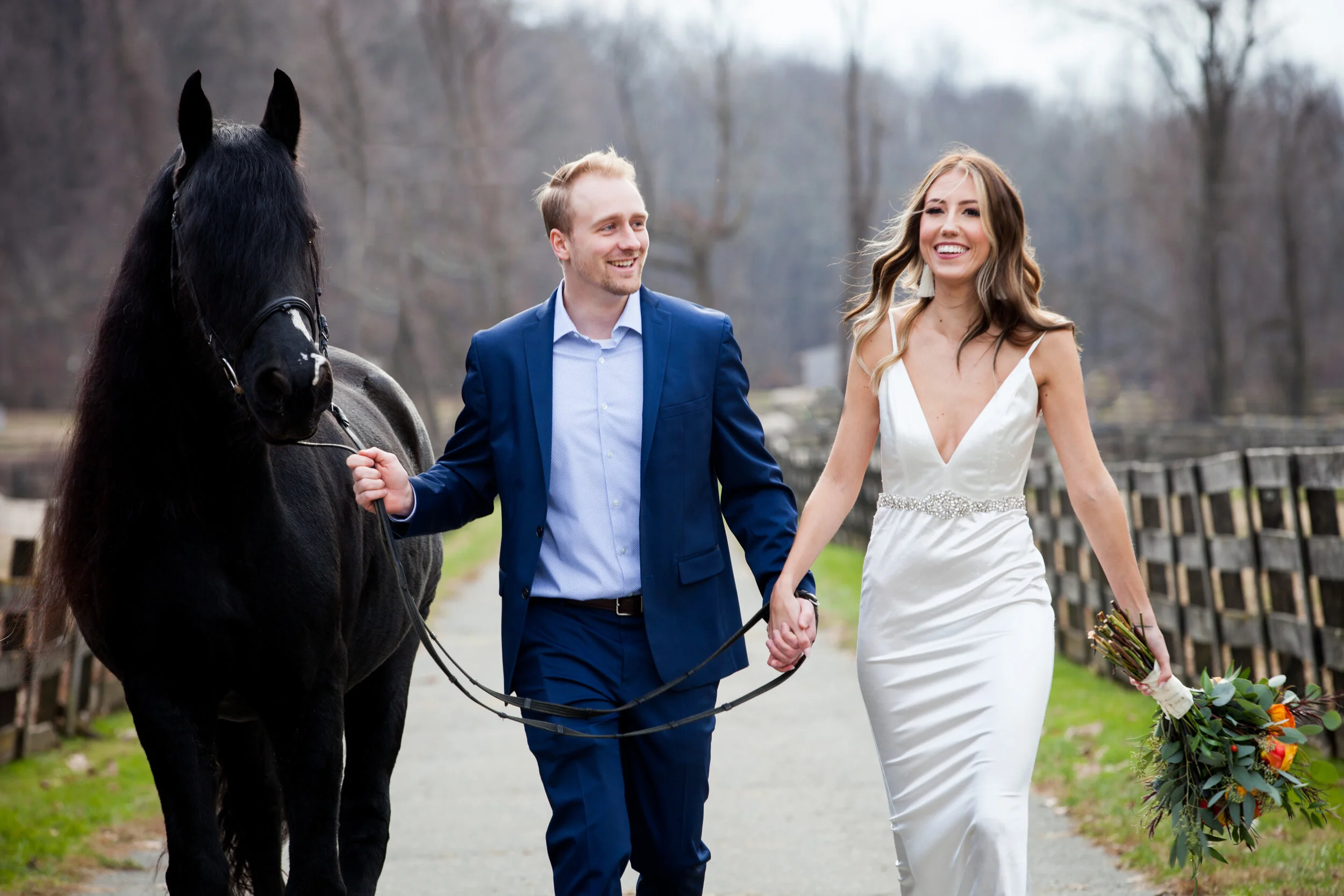 Couple in wedding attire walking with a black horse