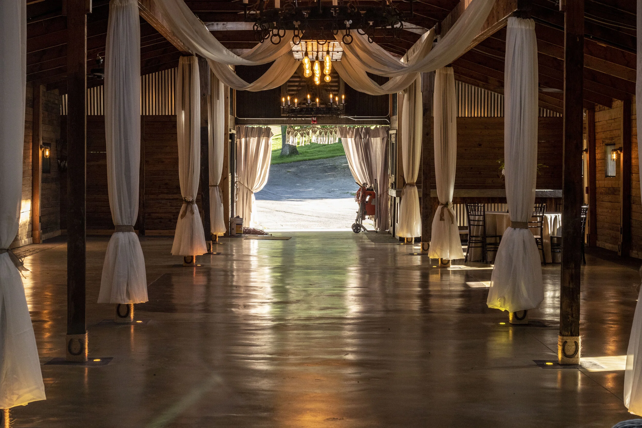 Interior of a rustic event venue with draped white curtains, wooden columns, and chandeliers