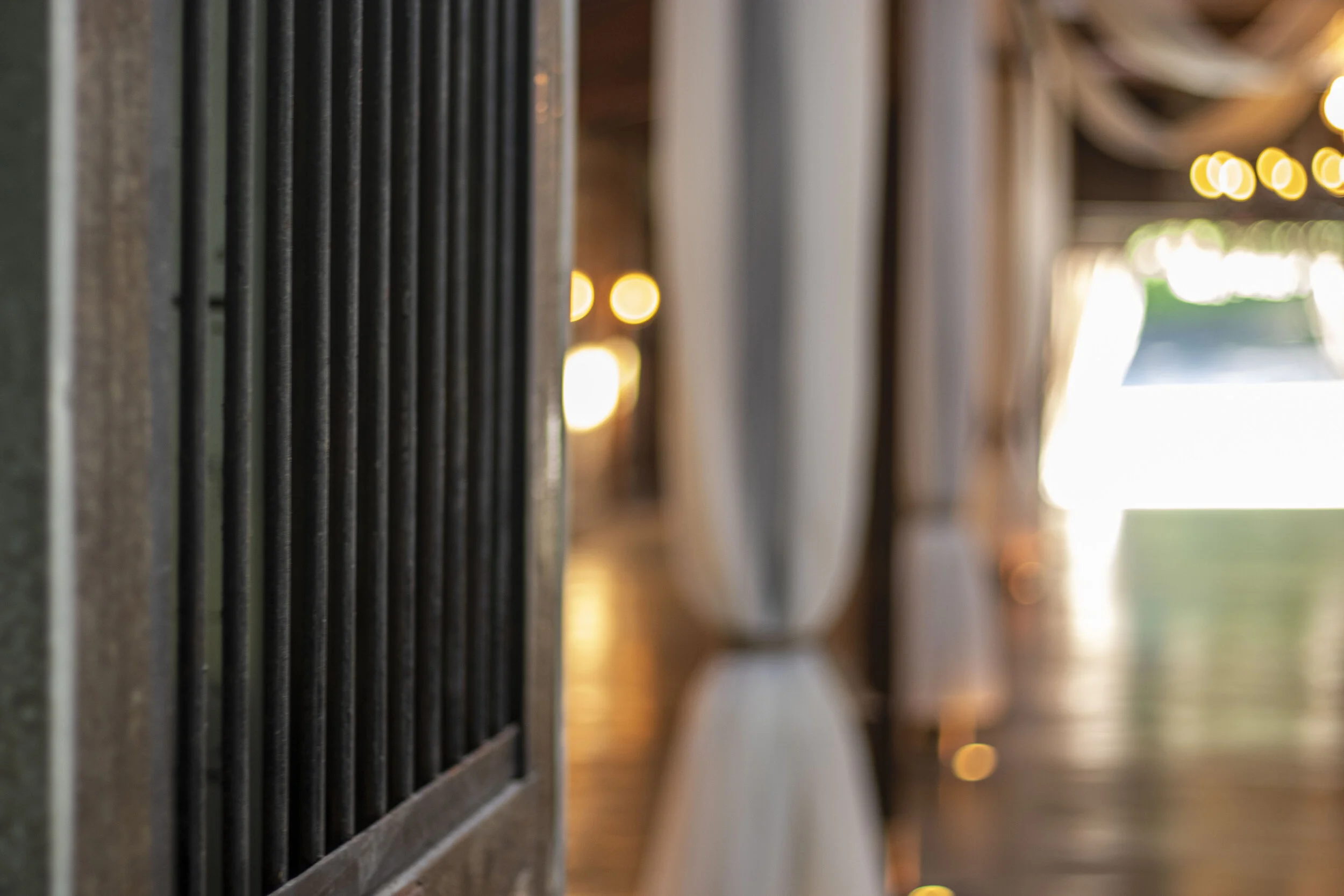 Close-up of a series of vertical black bars with blurred background of a well-lit, draped hallway.