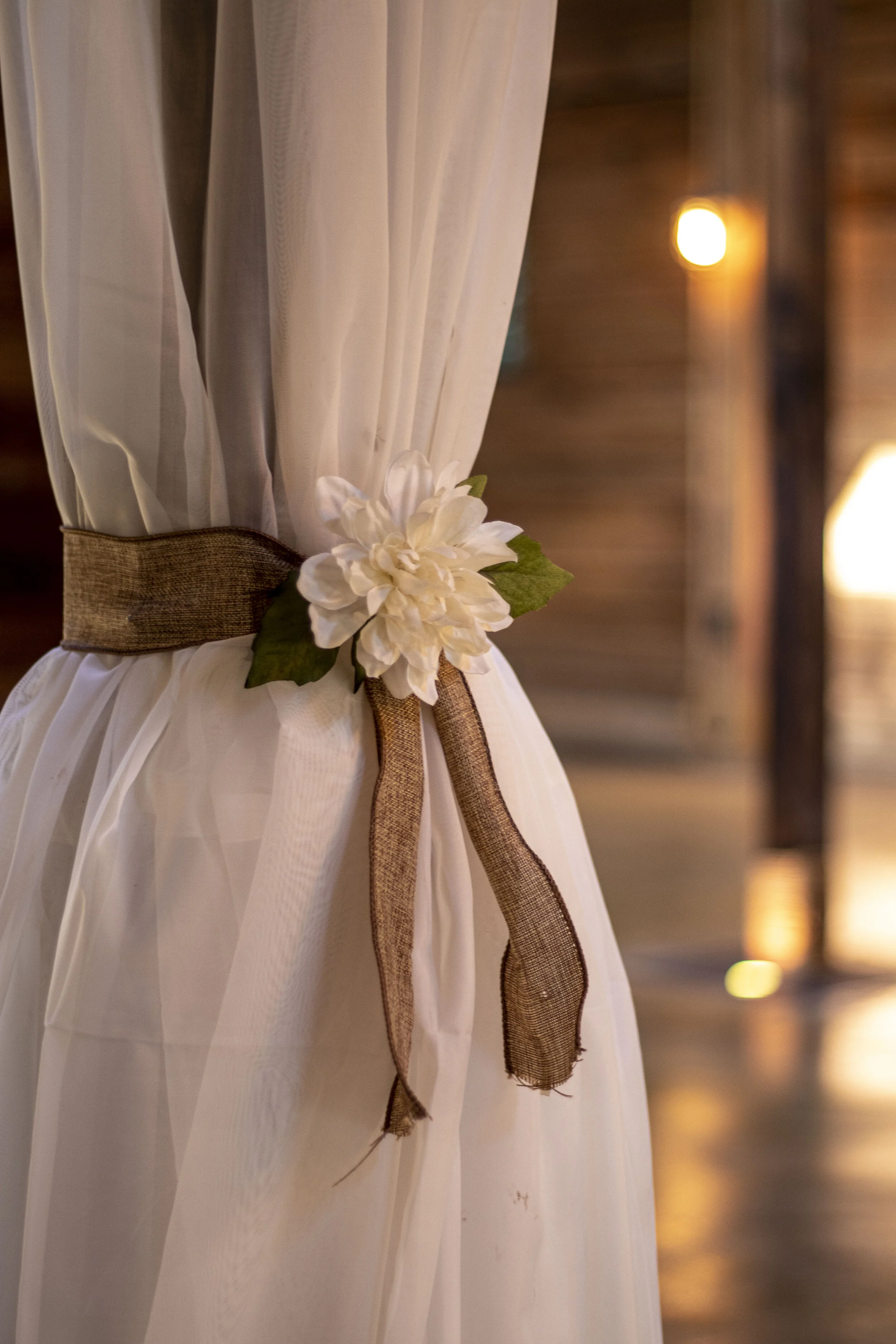 White curtain tied with a burlap ribbon and decorated with a white flower.