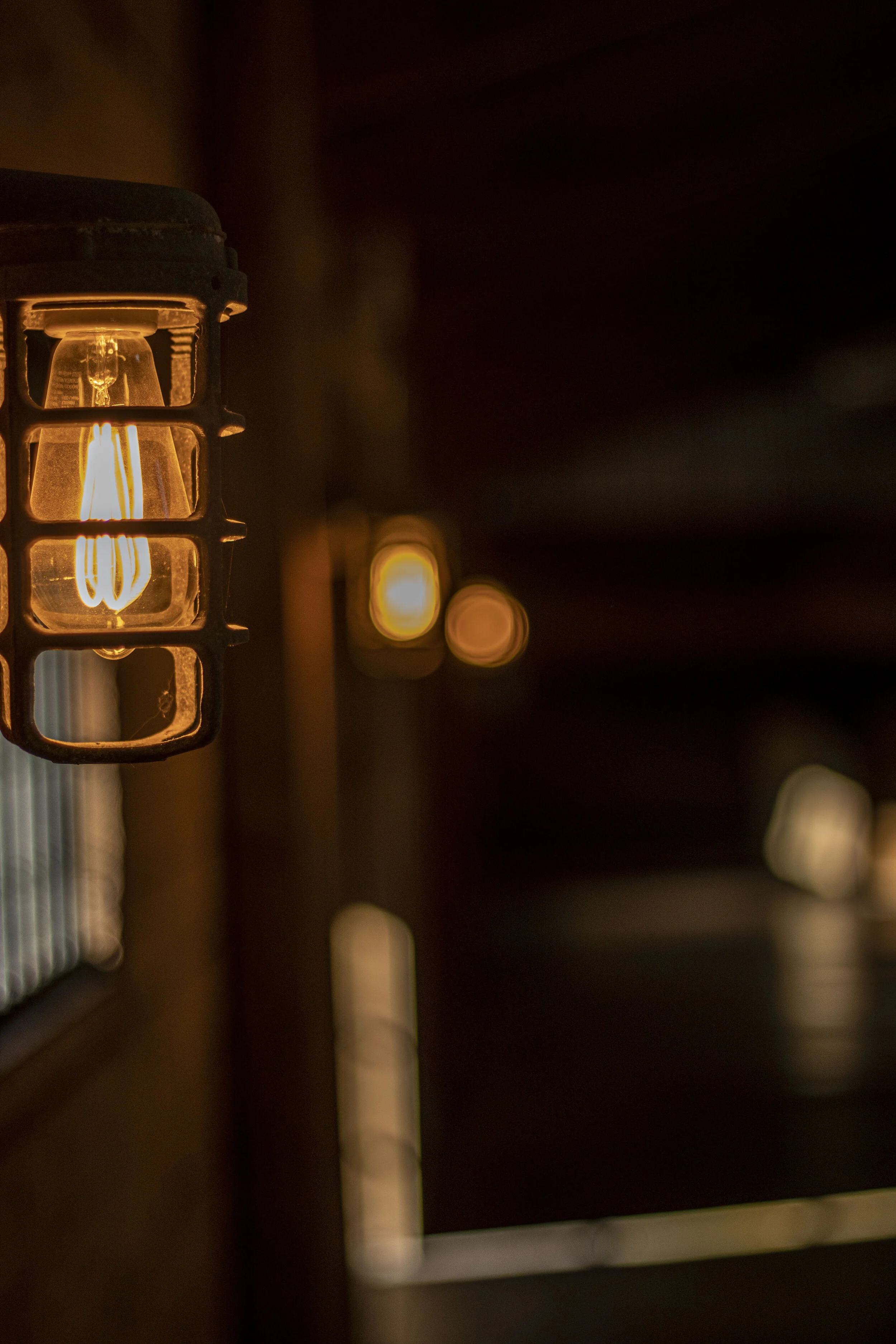 Dimly lit hallway with vintage-style wall lamps, featuring a glowing Edison bulb in foreground, creating a warm ambiance.