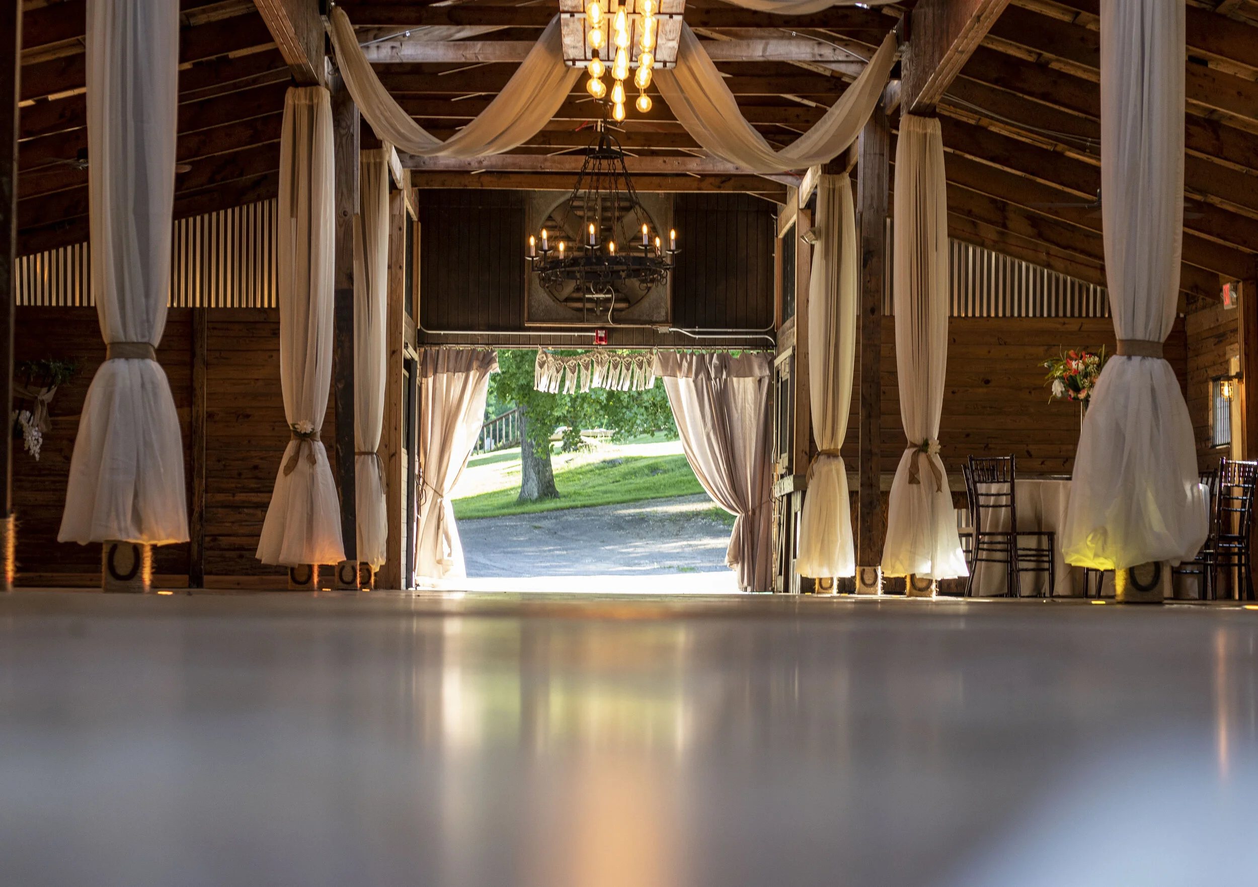 Interior of a rustic barn wedding venue with draped fabric and chandeliers, viewed from the floor.