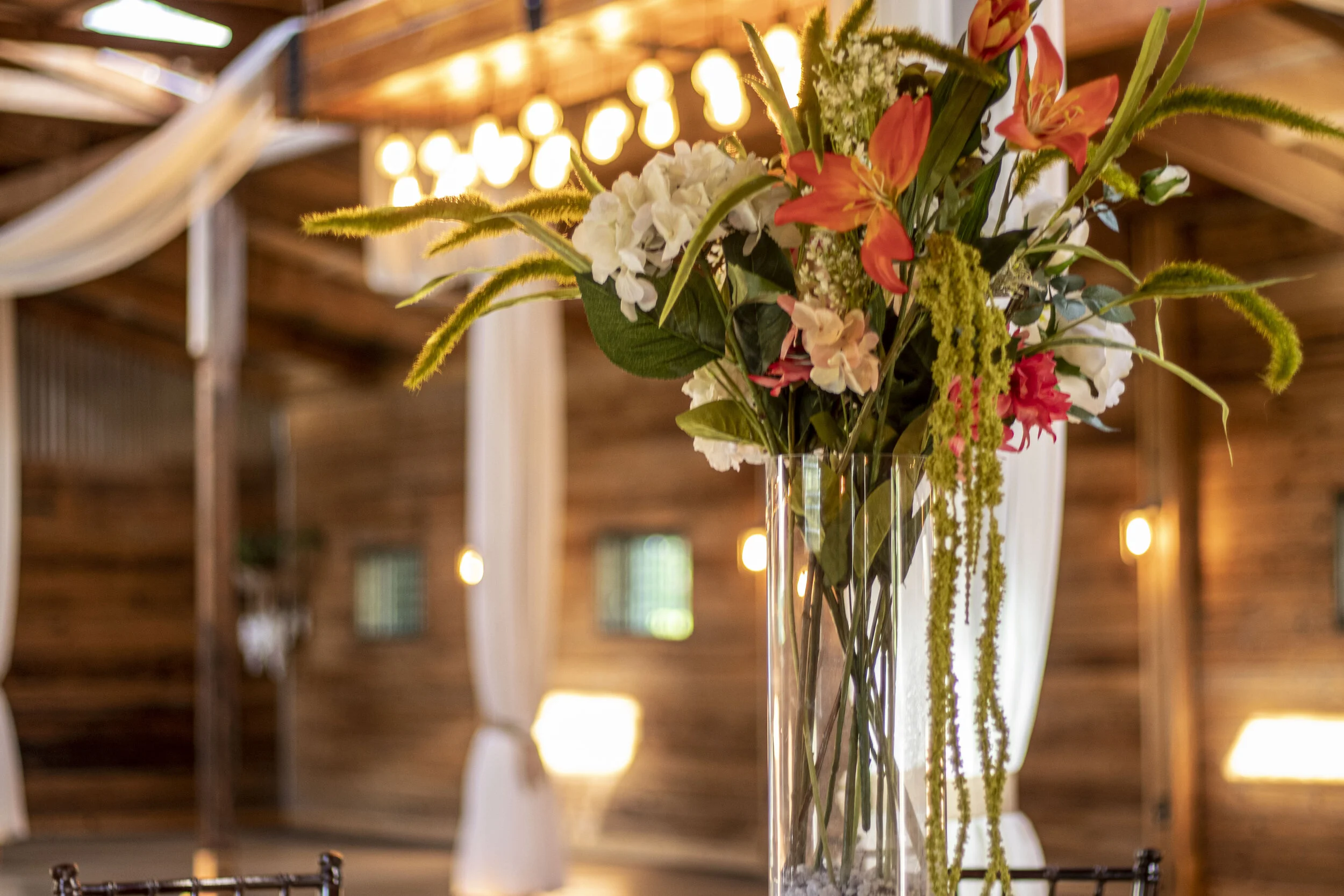 Floral arrangement in a rustic barn setting with wooden walls and draped fabric.