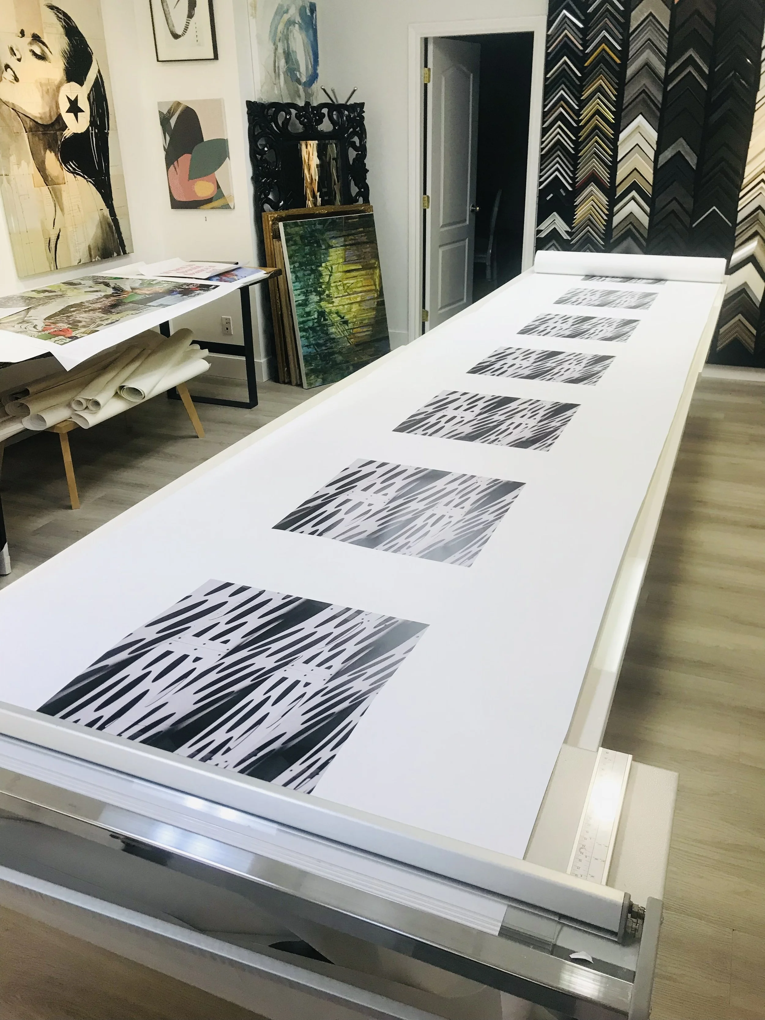 Minimalist interior with a wooden sideboard, two abstract black and white art prints, a white table lamp, a white chair draped with a beige blanket, a glass vase with yellowish plant stems, and a stack of books.