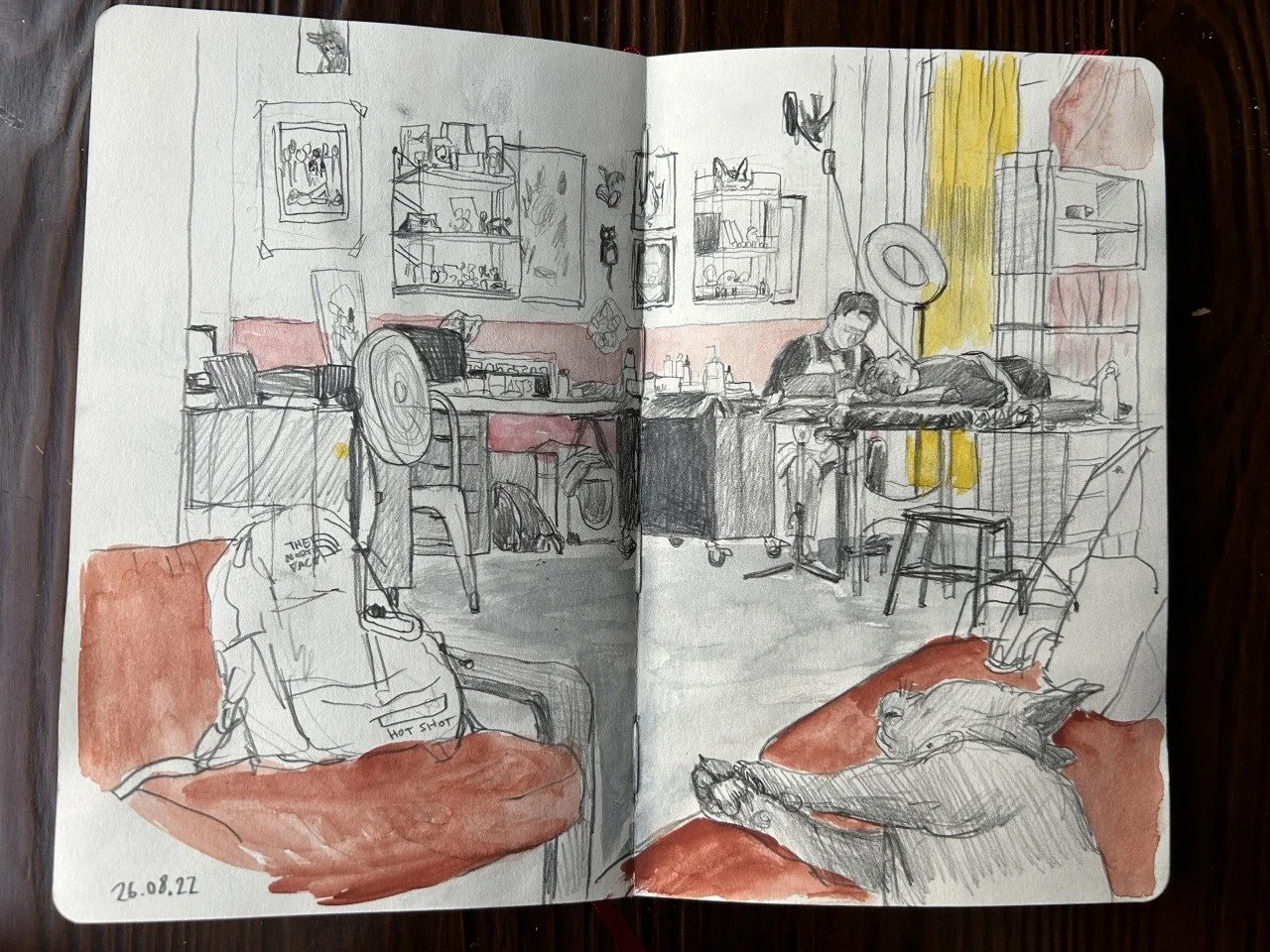 Skizze eines gemütlichen Raumes mit einem Hund auf einem roten Kissen, jemand arbeitet an einem Tisch, im Hintergrund sind Regale, Dekorationen und Fenster mit gelben Vorhängen, das Datum 26.08.22 ist in der Ecke zu sehen.
