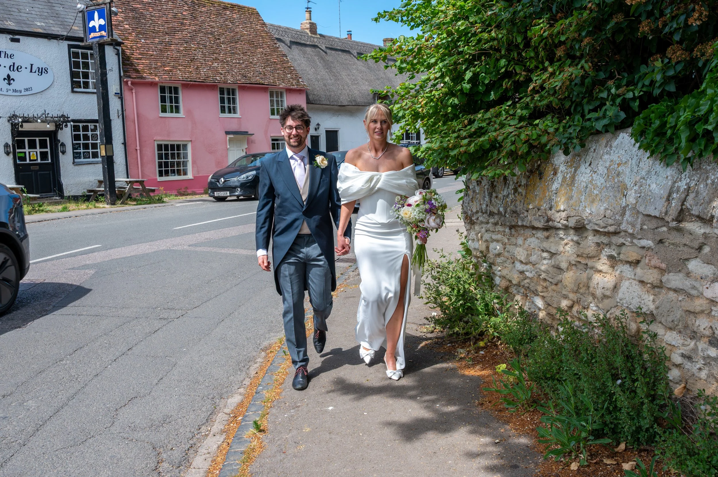A bride and groom hold hands and walk along one of Dorchester's side streets