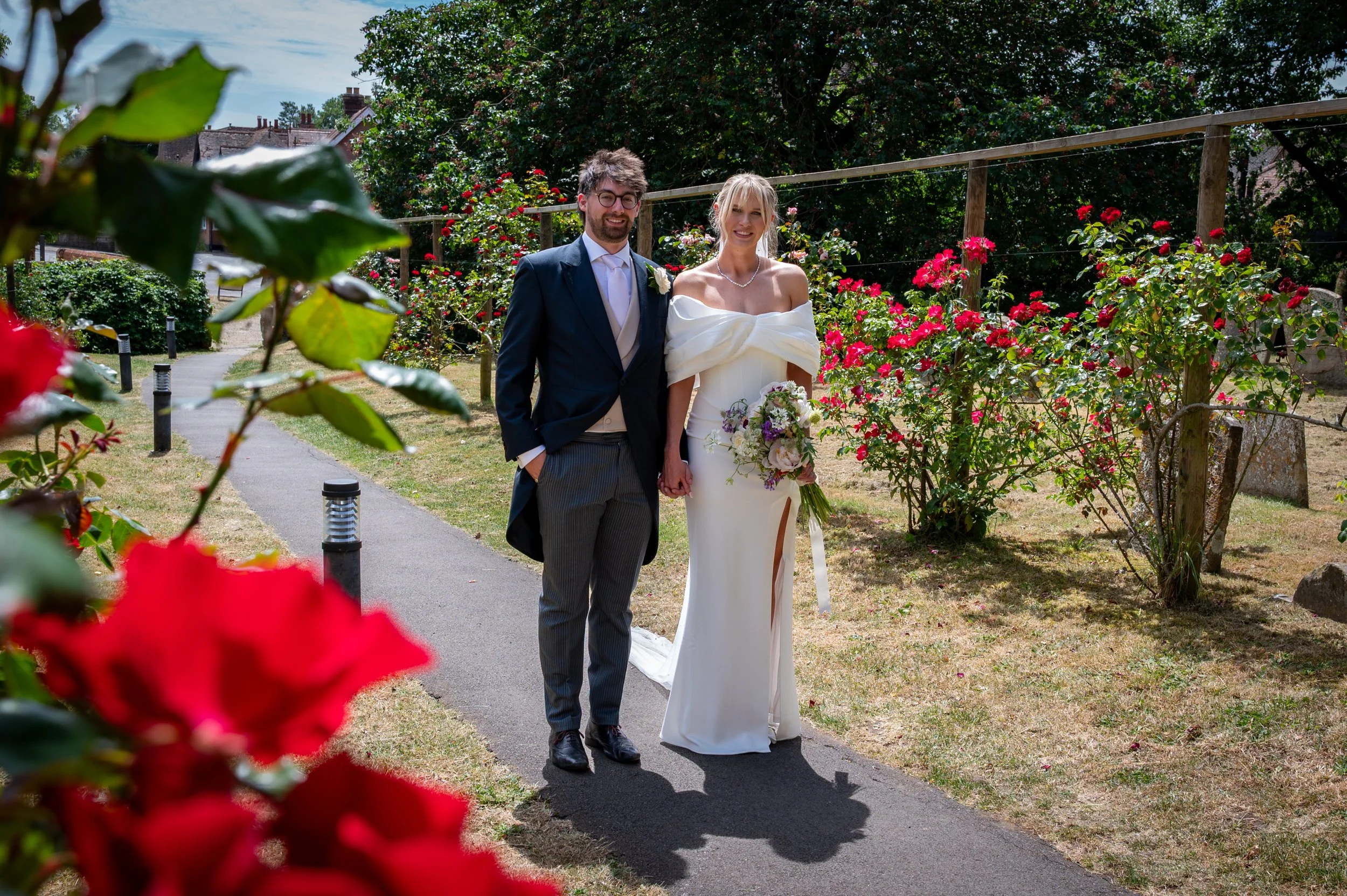 A Bride and Groom hold hands next to a rose lined entrance into Dorchester Abbey Oxfordshire