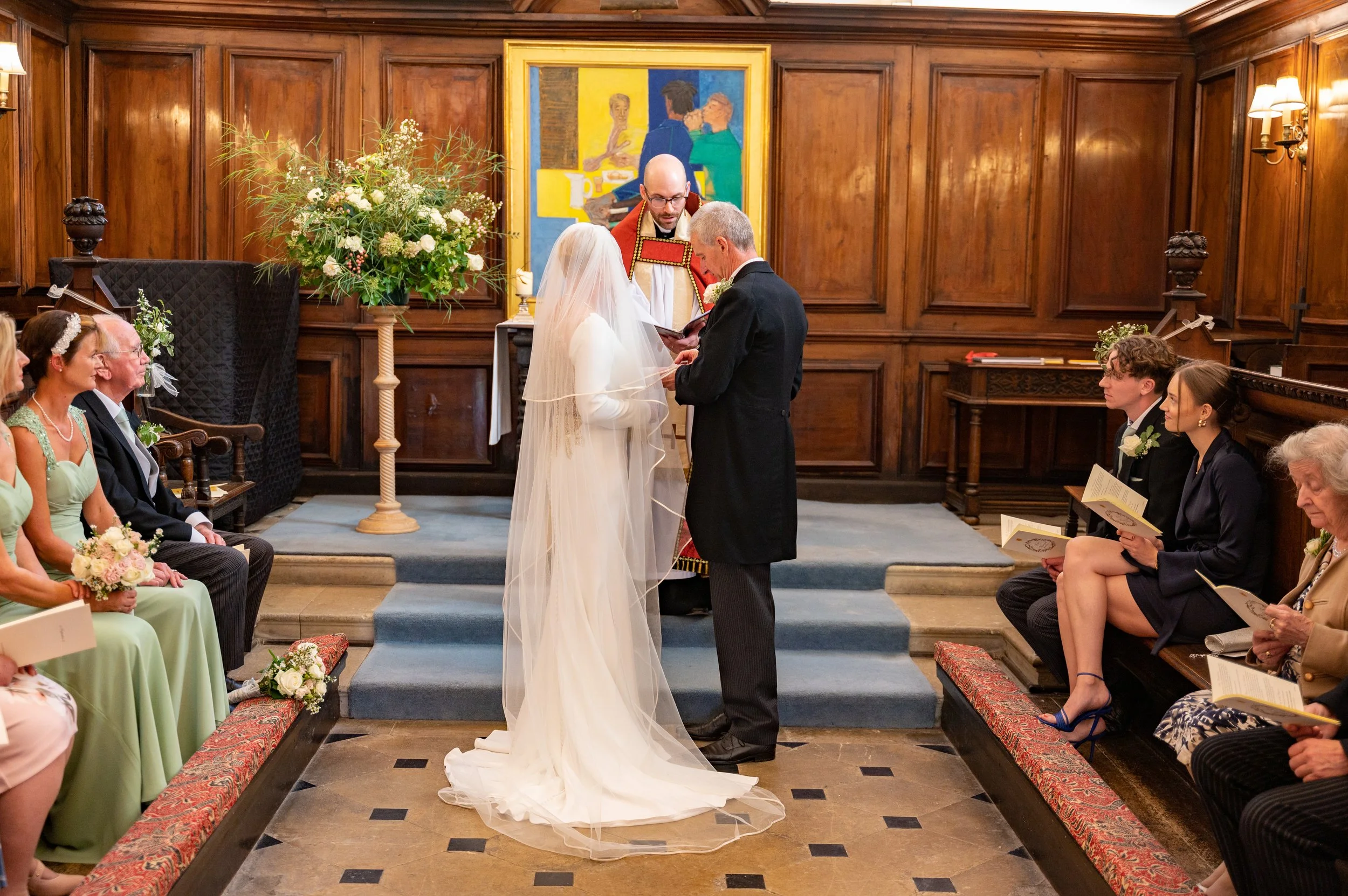 A bride and groom stand at the alter with the vicar conducting their ceremony watched by guests