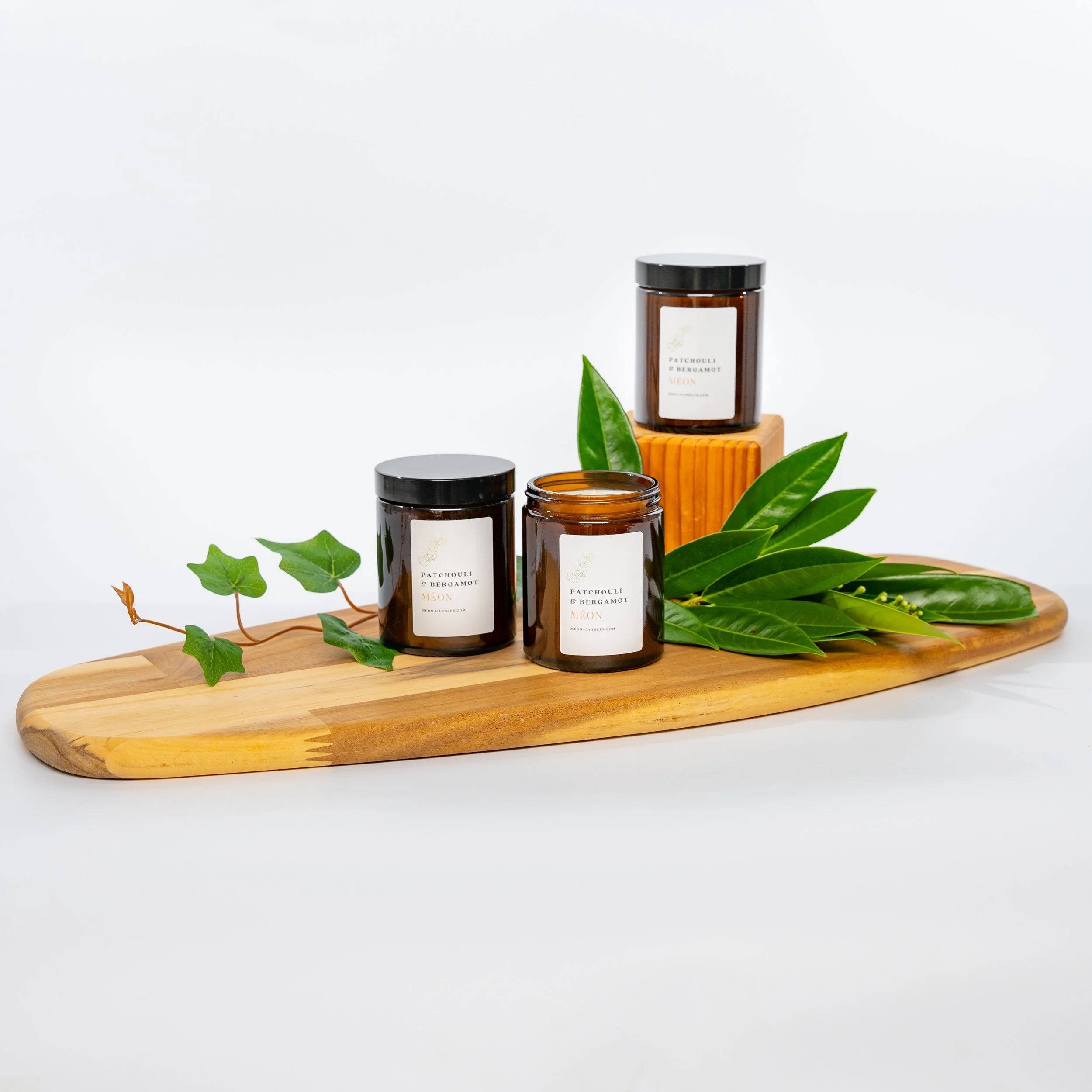 Three candles labeled 'Patchouli & Bergamot' with green leaves on a wooden tray.