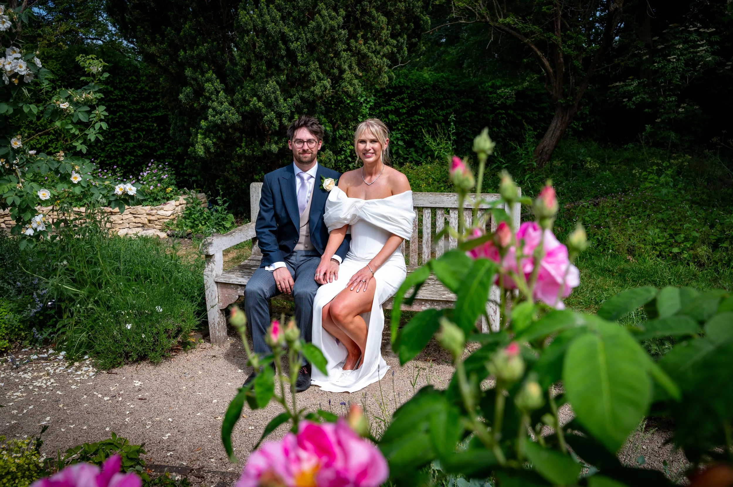 a bride and groom sit in a rose filled garden at Dorchester Abbey in Oxfordshire