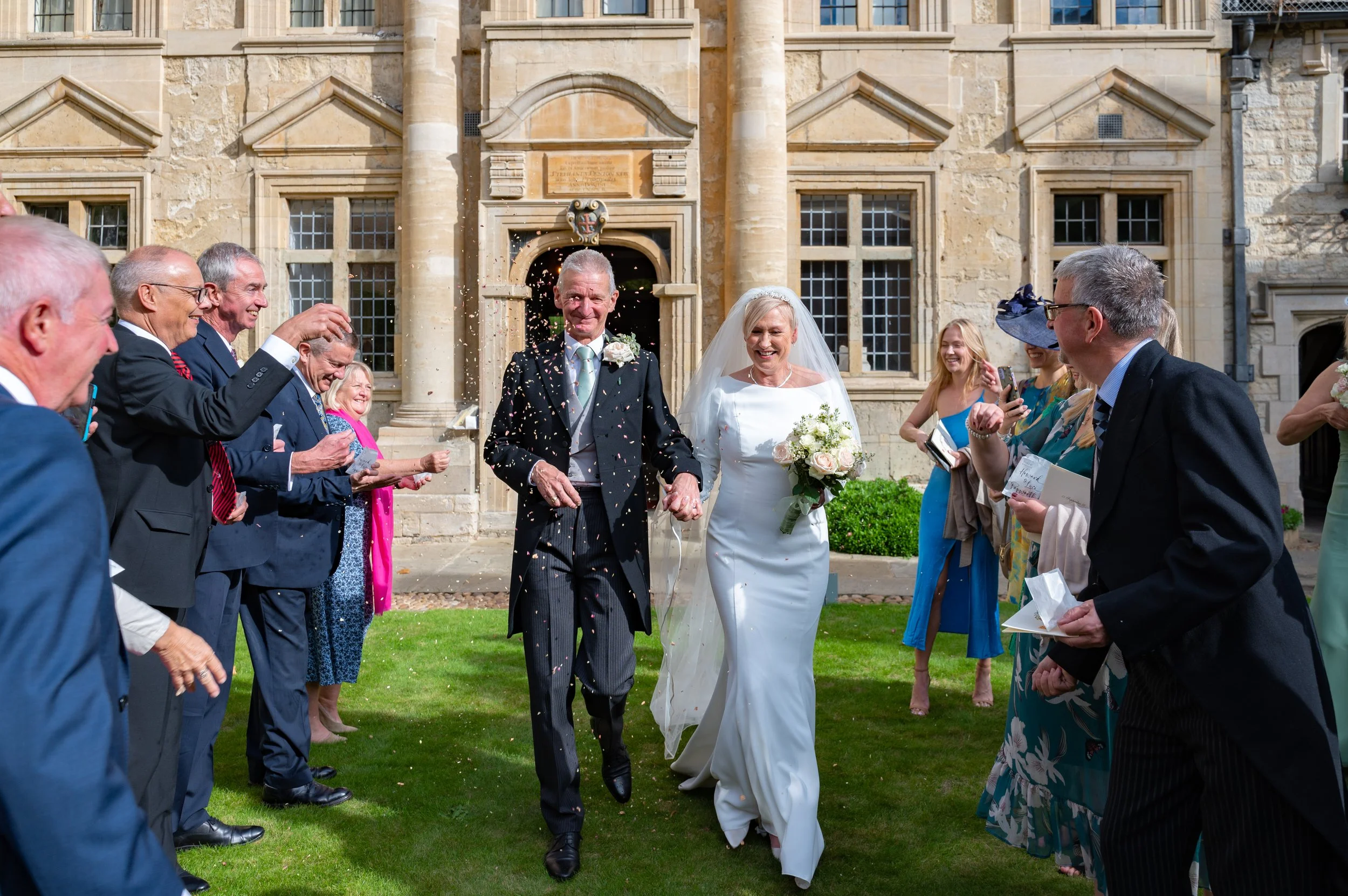 A bride and groom walk through a confetti shower during their Oxford University wedding
