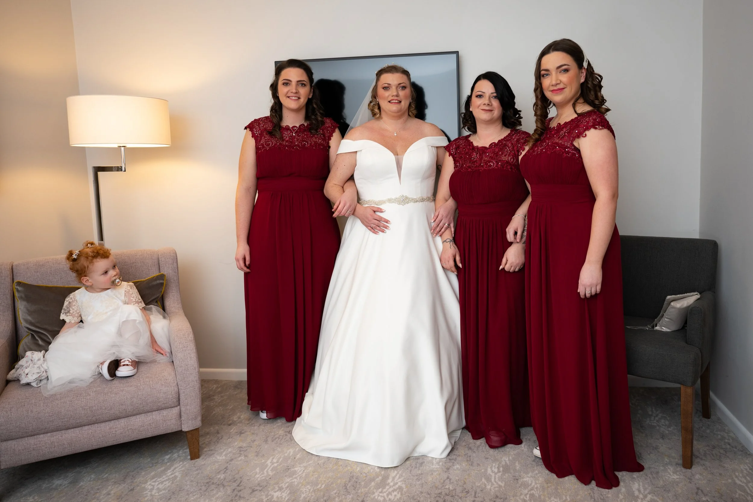 a bride and her bridesmaids stand next to one another with a young bridesmaid looking on