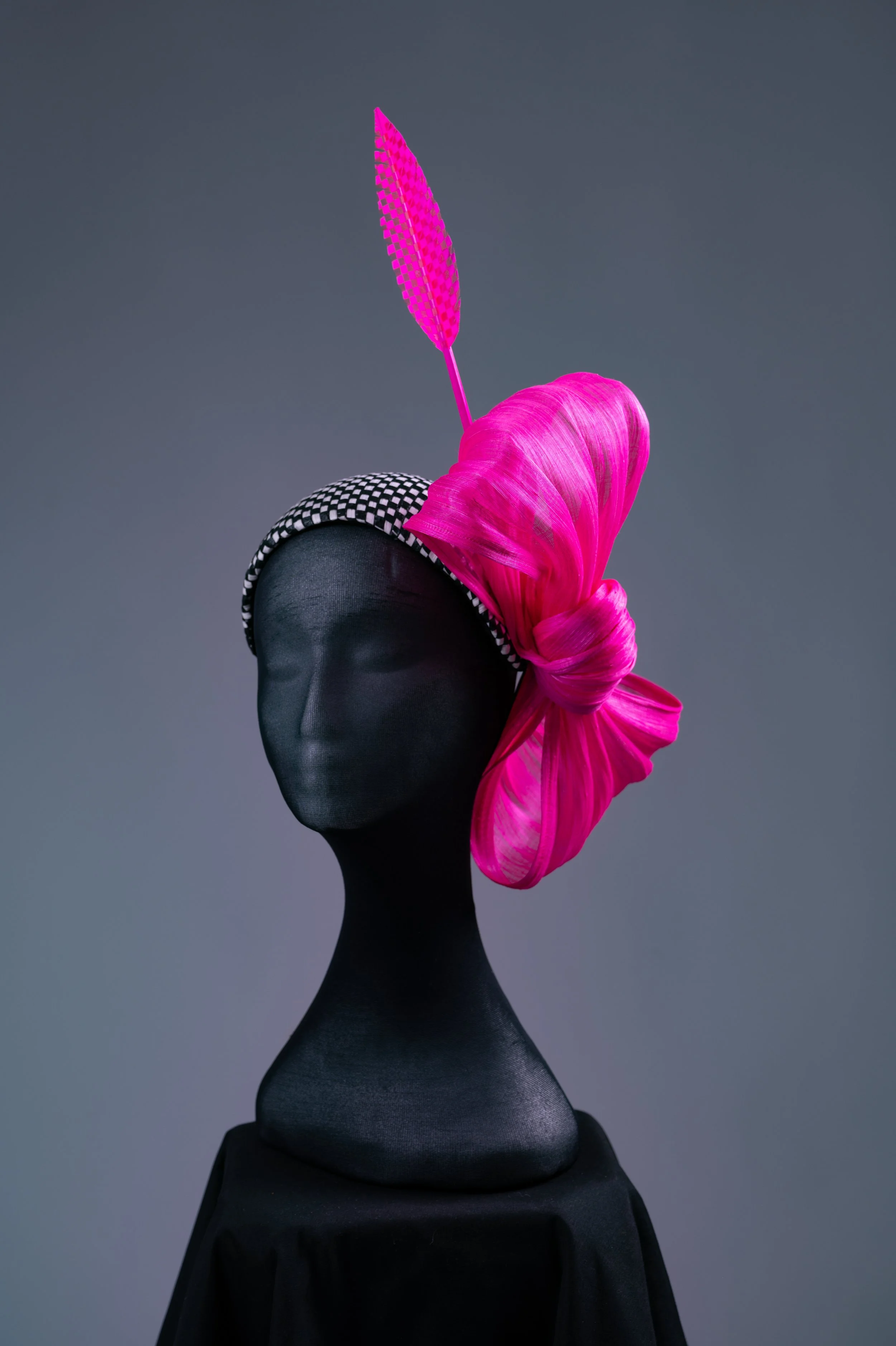 A black and white chequered fascinator with a pink bow on a mannequin head