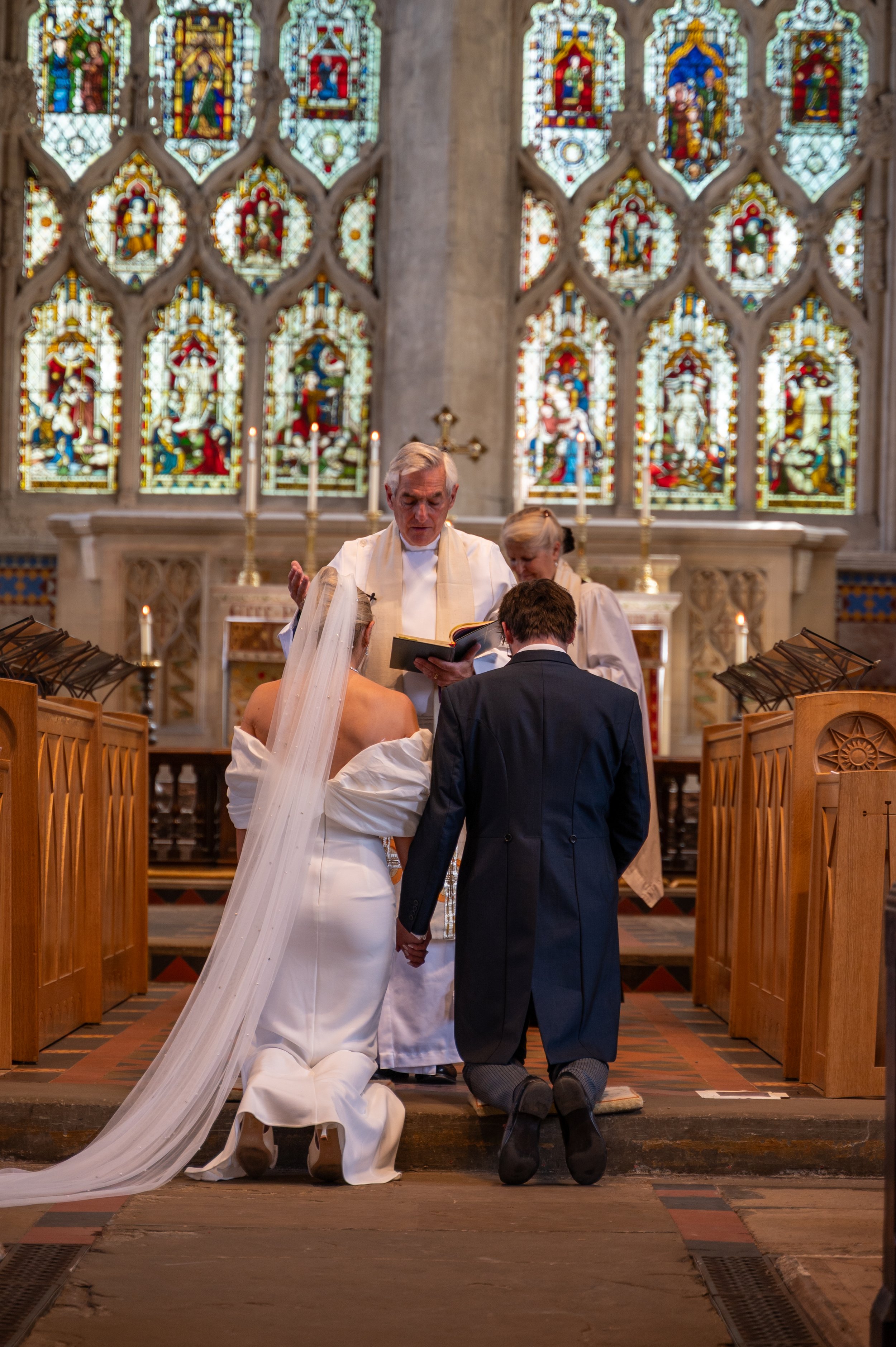 A bride and groom kneel before the vicar during their wedding ceremony at Dorchester Abbey