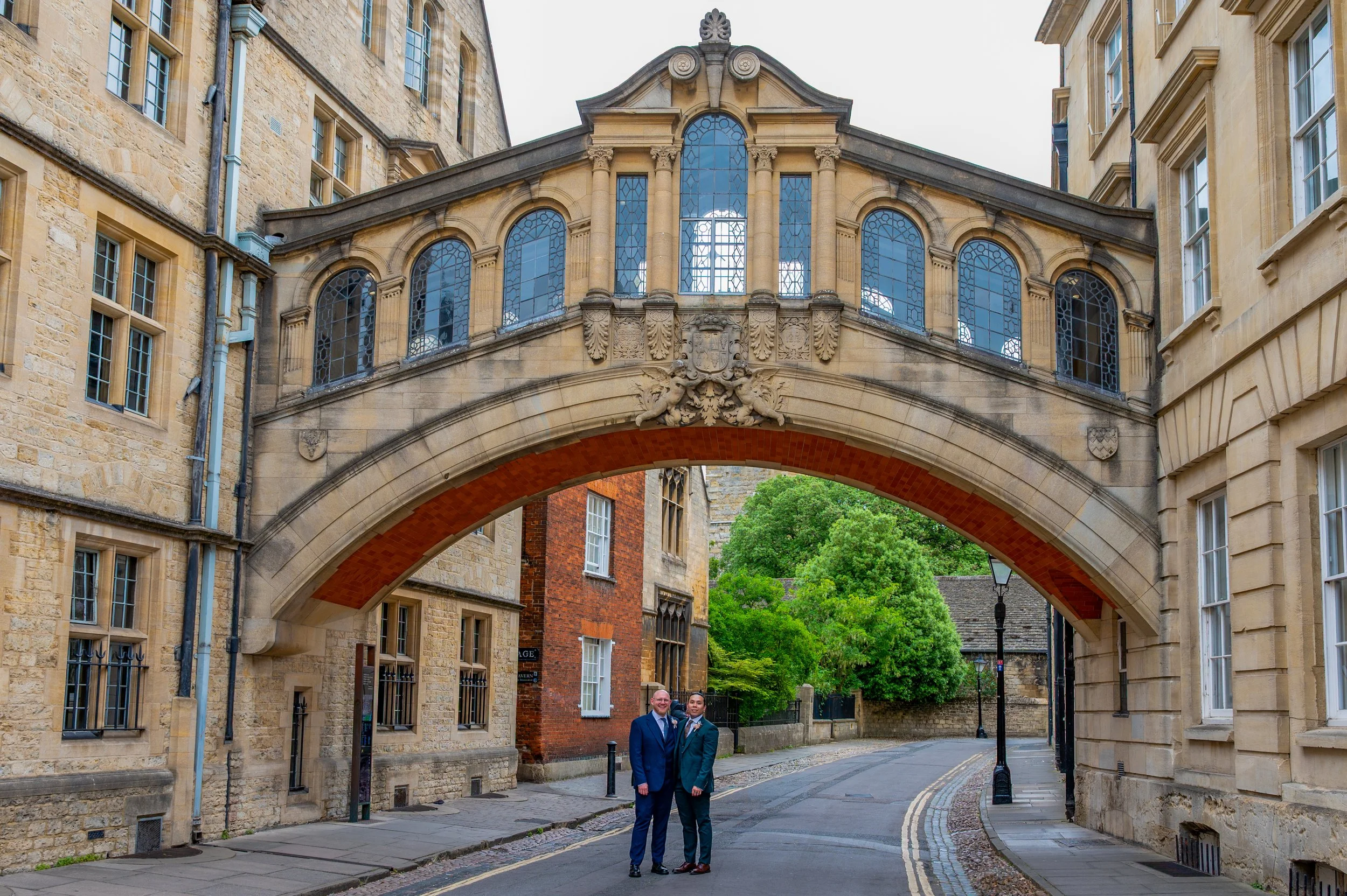 a same sex couple stand under the Bridge of Sighs in Oxfordshire