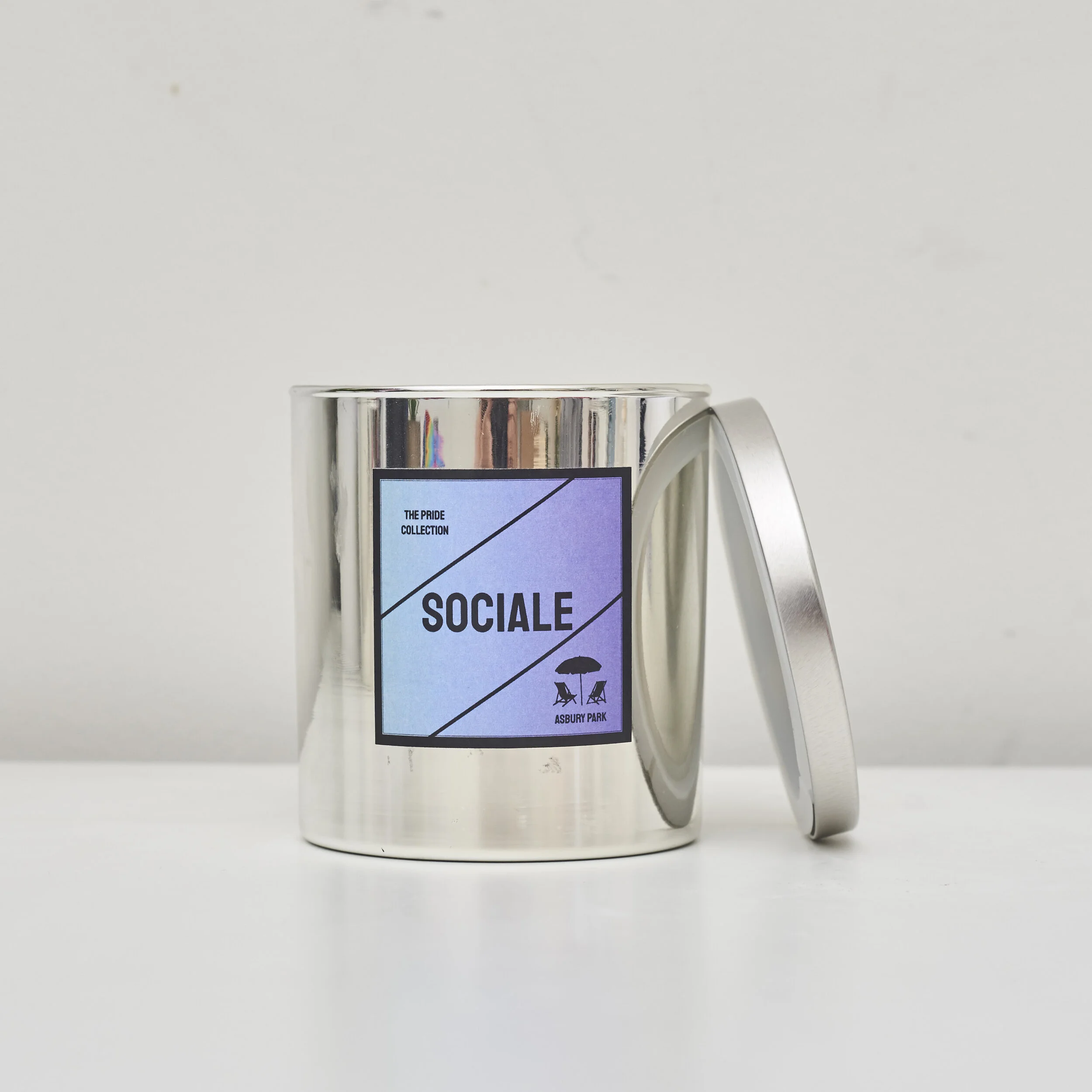 Silver candle jar labeled "SOCIALE" from the Pride Collection by Asbury Park, with the lid partially open.