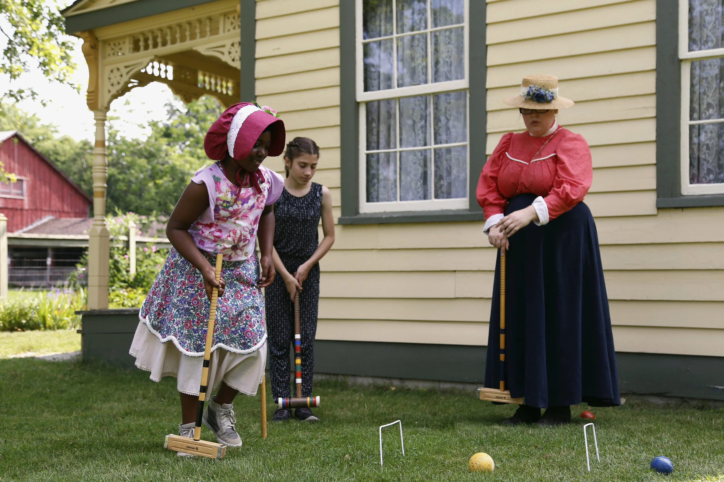 Two children and an adult playing croquet outside of a yellow house, Peel House.