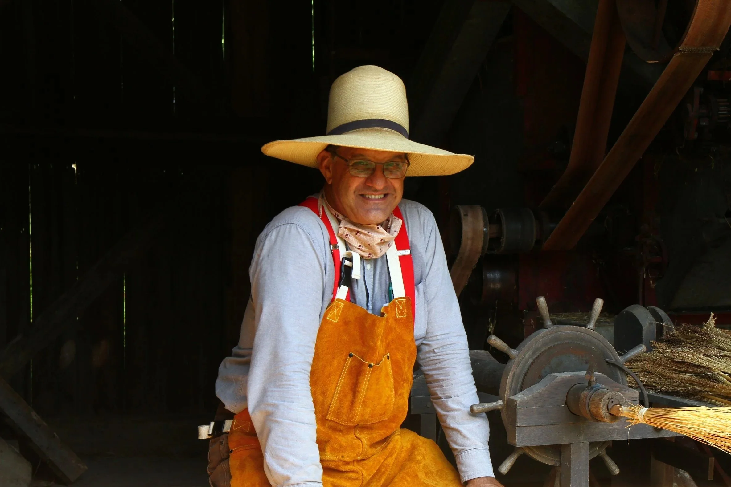 A photo of a middle-aged man in a tradesman costume, which includes a leather apron and a wide sun hat.