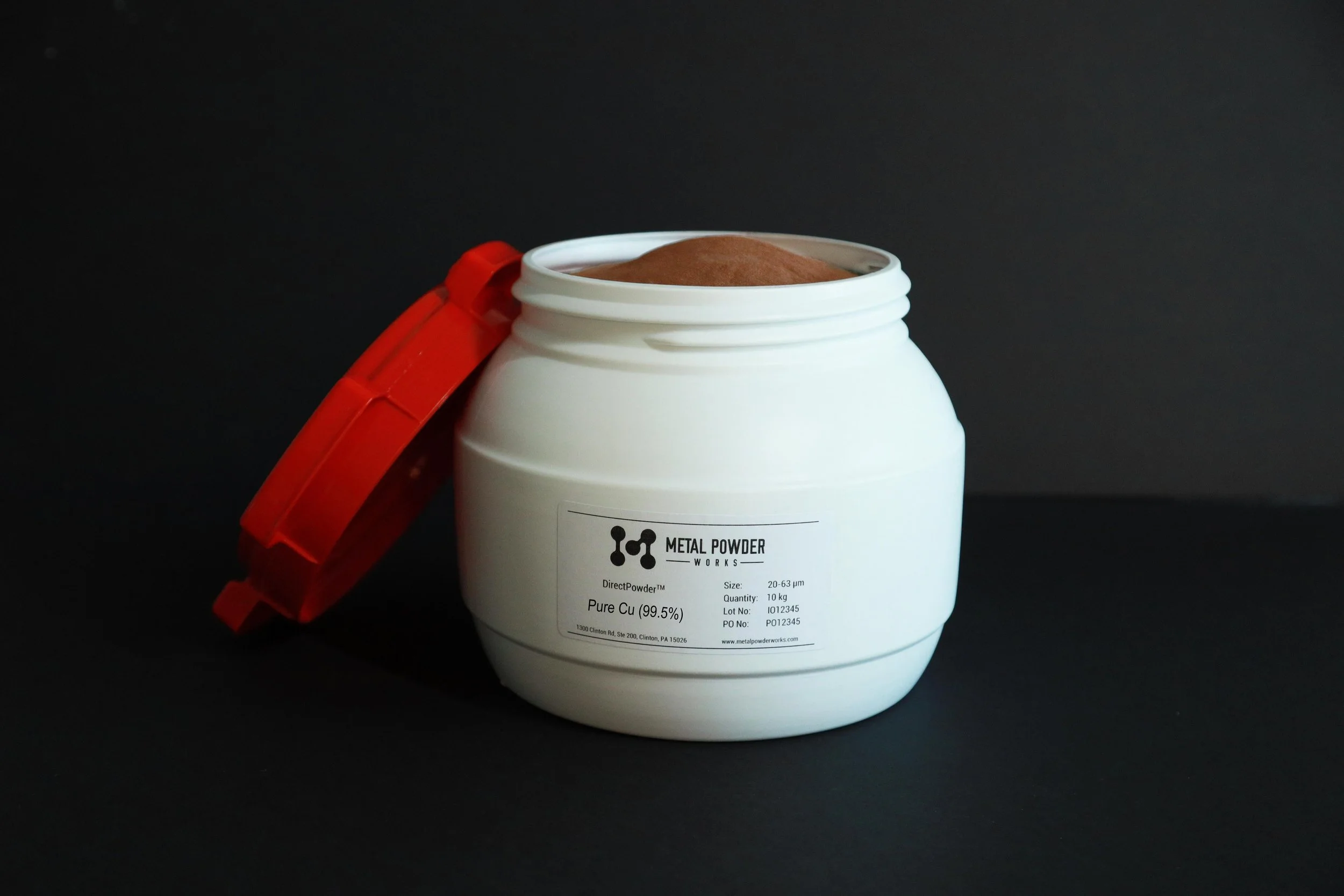 A white plastic container of metal powder with a red lid, open to show brown powder inside, set against a black background.