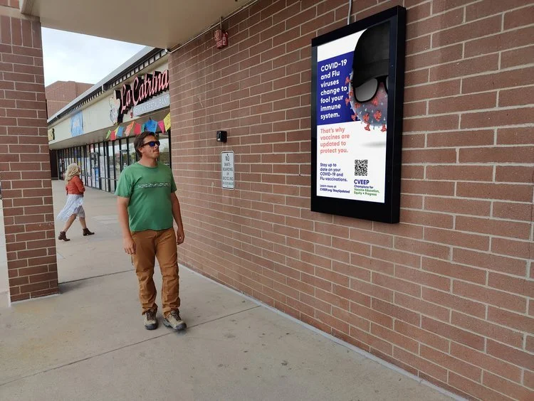 Man walking past a COVID-19 vaccine awareness poster on a brick wall outside a store.