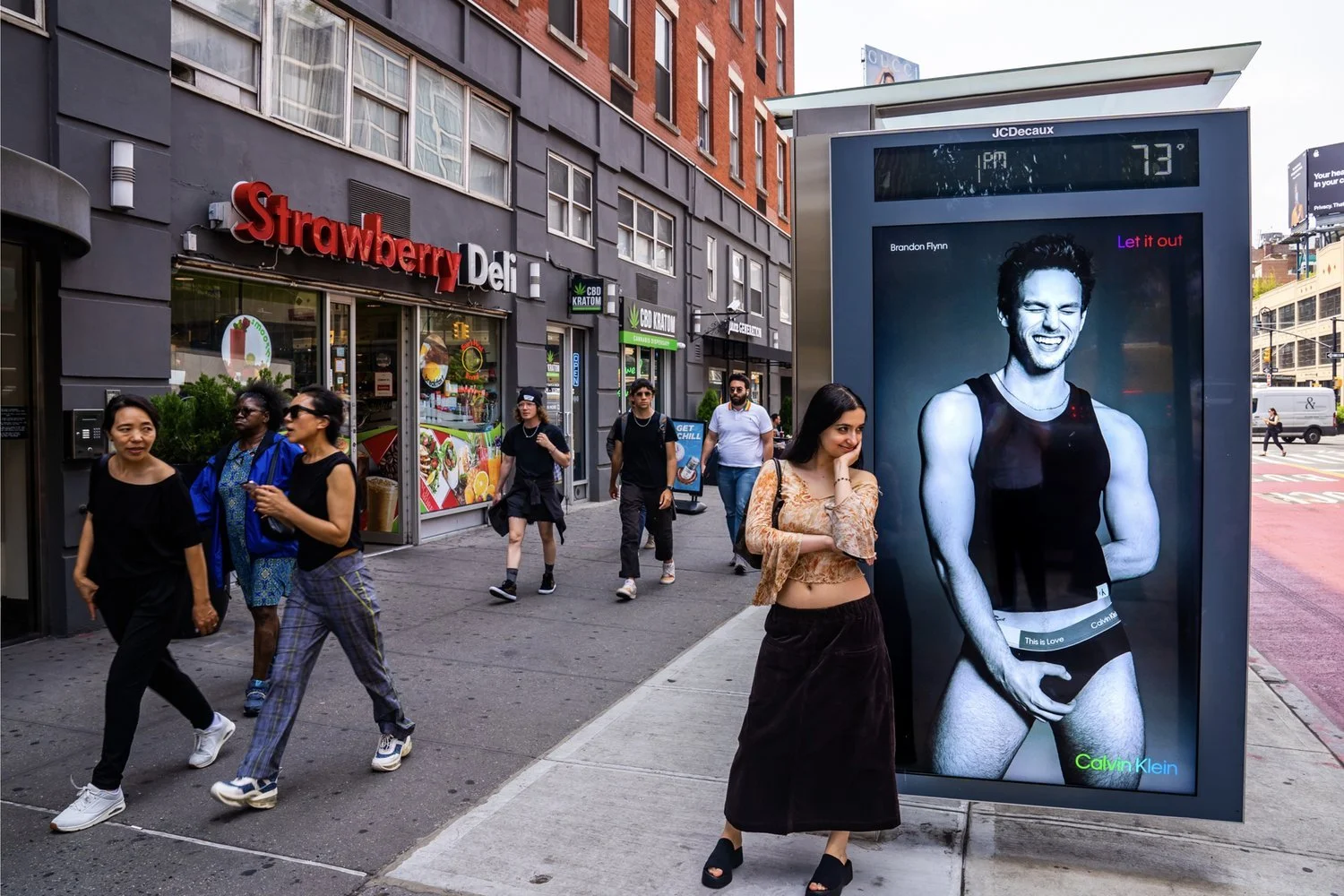 City sidewalk with pedestrians, large Calvin Klein underwear ad, and Strawberry Deli storefront.