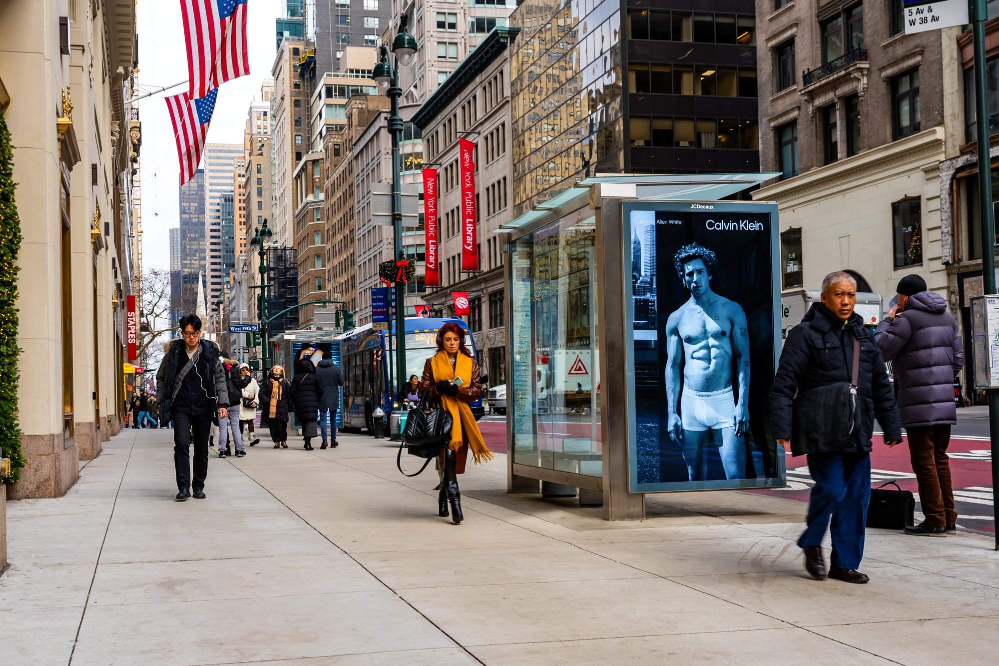 City street scene with pedestrians, large Calvin Klein advertisement, American flags, and high-rise buildings.
