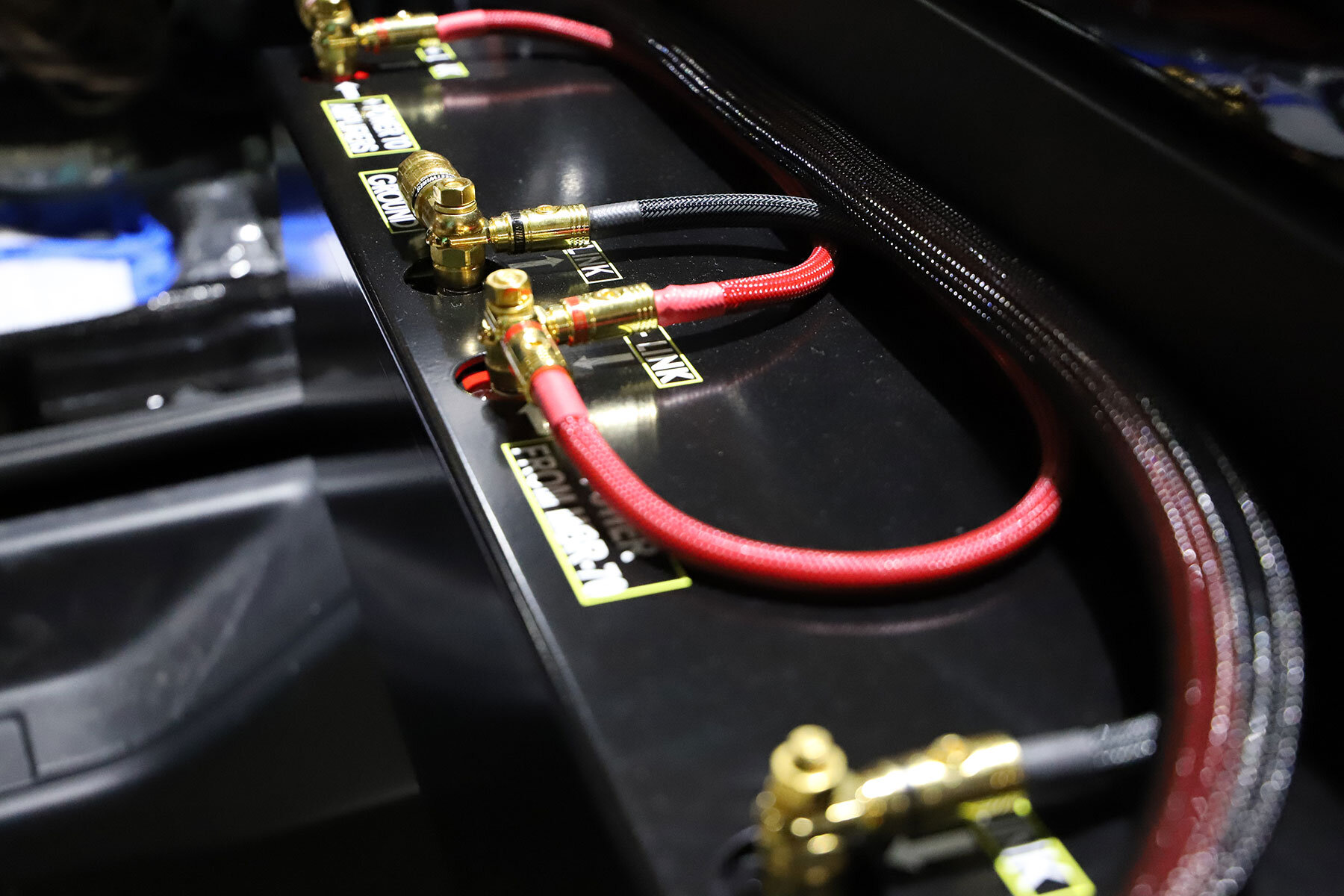 Close-up of a car battery with labeled terminals and colored cables connected.