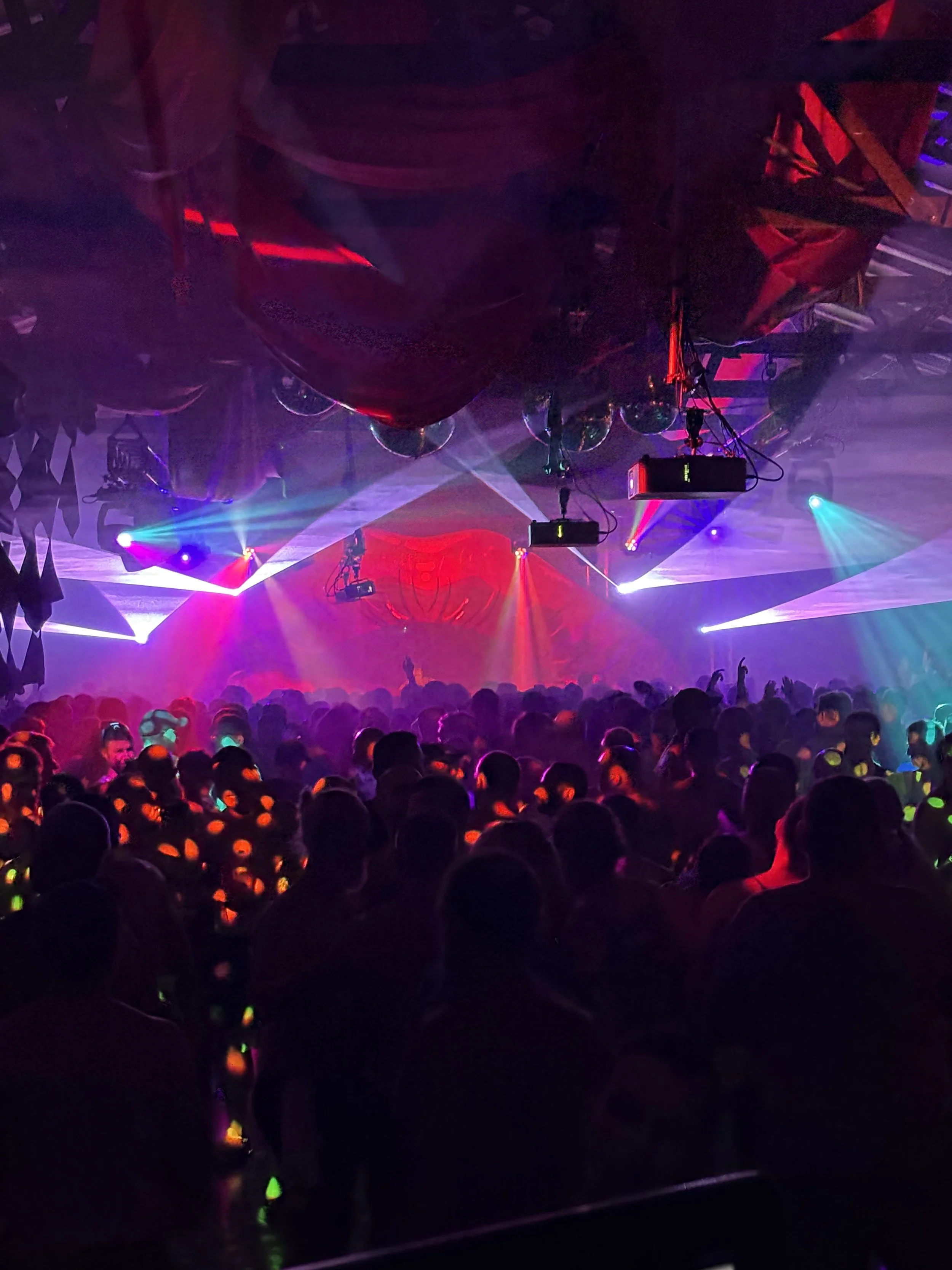 Crowded dance floor at a nightclub with colorful stage lights and fog effects.
