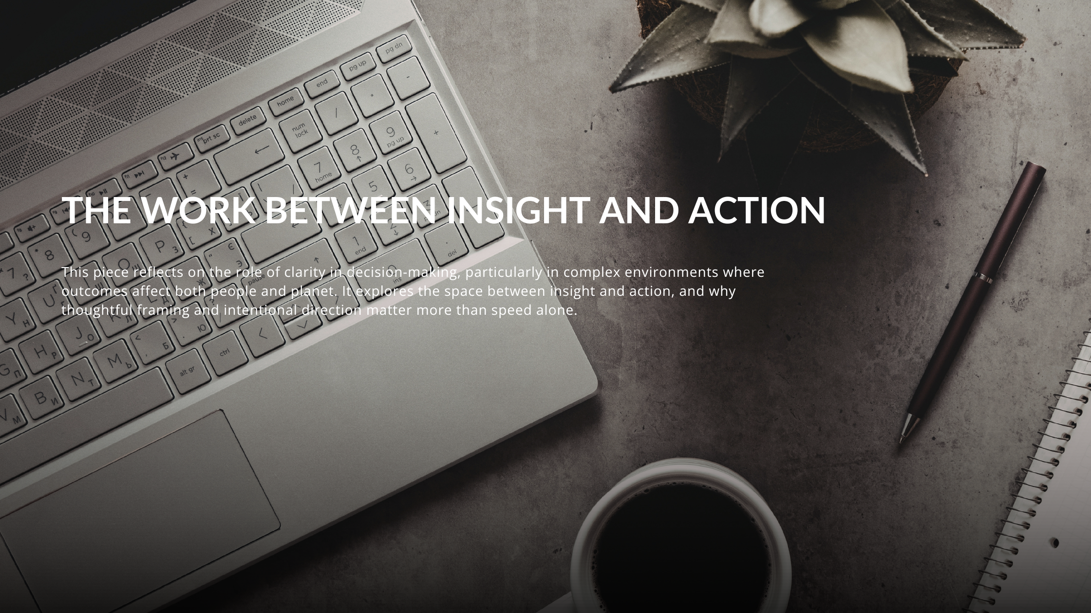 Birds-eye view of an open laptop beside a notebook and a small desk plant on a light workspace.