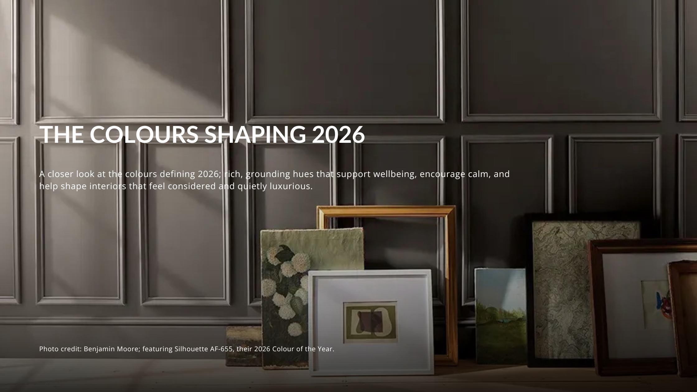 Benjamin Moore Silhouette AF-655, their 2026 Color of the Year, shown on a classic wall with decorative panel molding. Trending paint color display for interior design featuring art prints and empty gold frames.