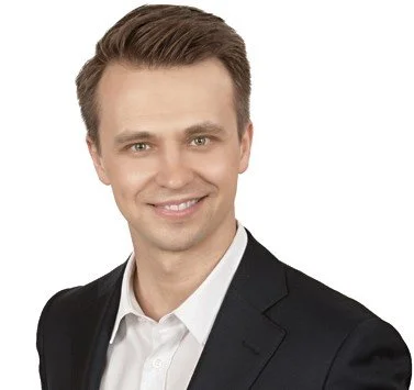 Nuori mies pukeutuneena pukuun ja hymyilevä kameralle.