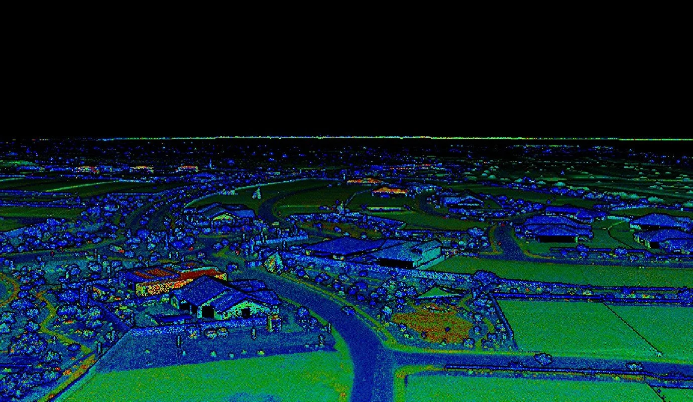 Aerial view of a small town with houses, roads, and green fields at night, illuminated by a drone or satellite.