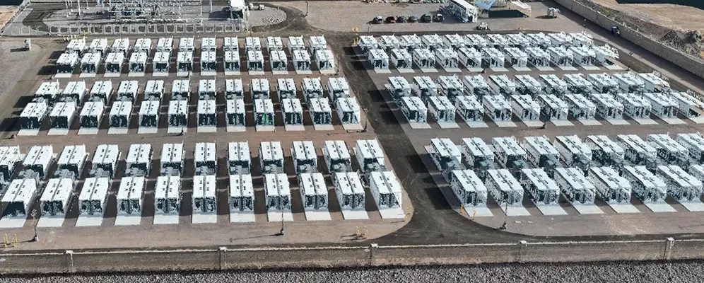 An aerial view of a large parking lot filled with white buses and vans, organized in rows on a paved surface, with some recent construction or paving work visible.