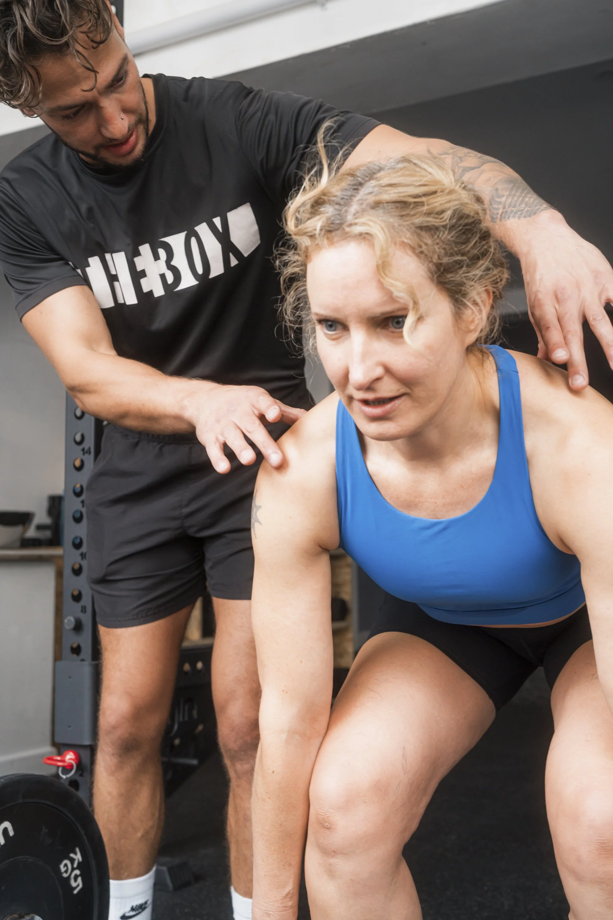 A coach helping a woman with weightlifting training in a gym. In Brighton at TheBox