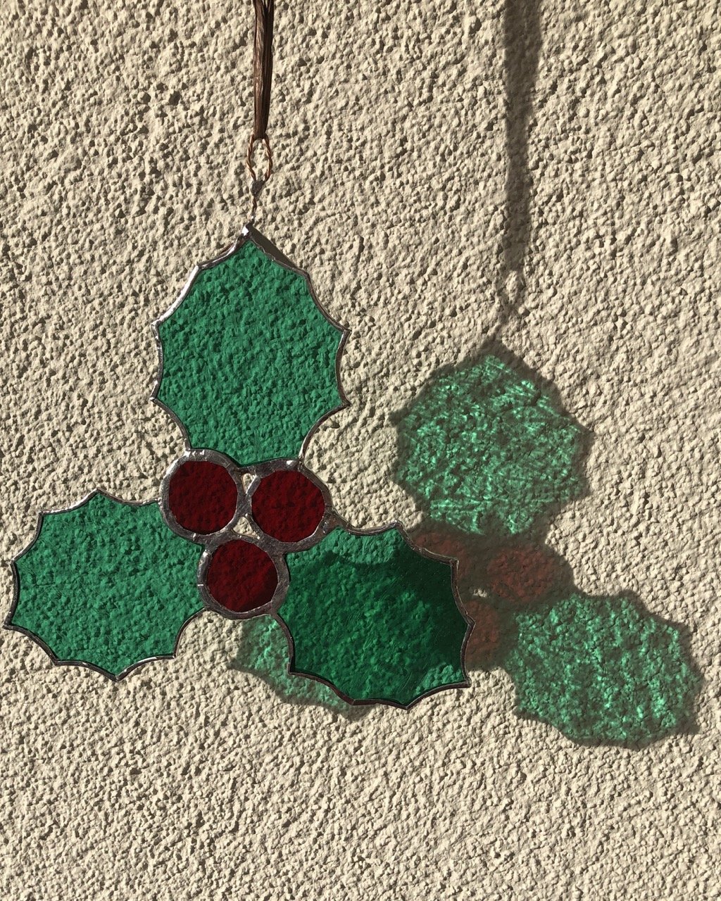 A stained glass sun catcher which depicts three glass holly leaves and three glass holly berries soldered together as a Christmas decoration
