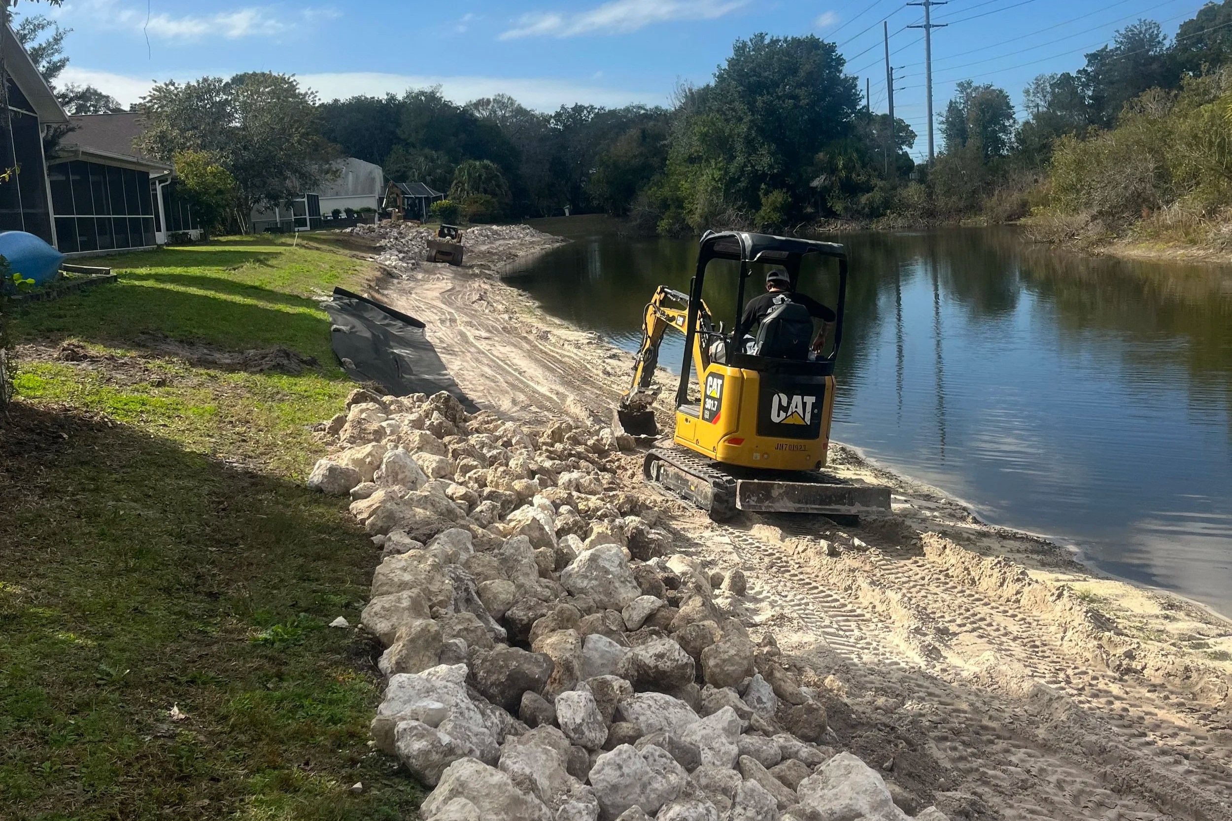 Excavator placing rip rap along eroded pond embankment