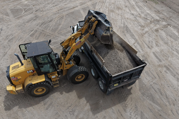 A yellow Caterpillar backhoe loader loading dirt into a black dump truck on a construction site.