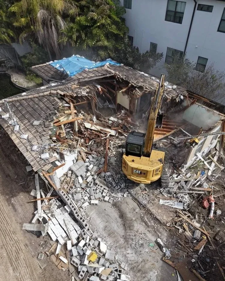 Construction excavator demolishing a building with debris scattered around.