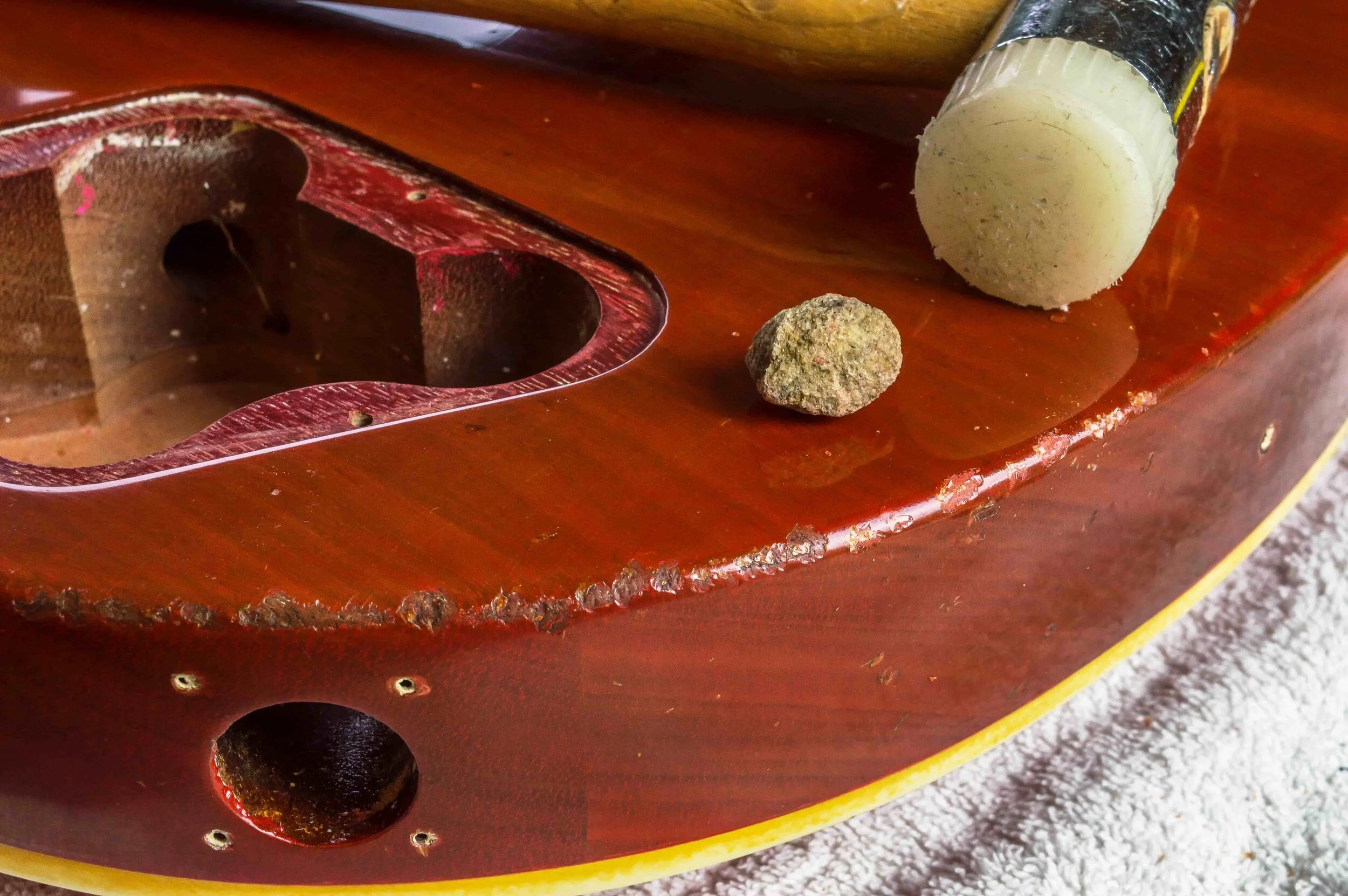 A stone and mallet are used to chip lacquer along the edge of the body and the area on the left has been stained and wax polished.